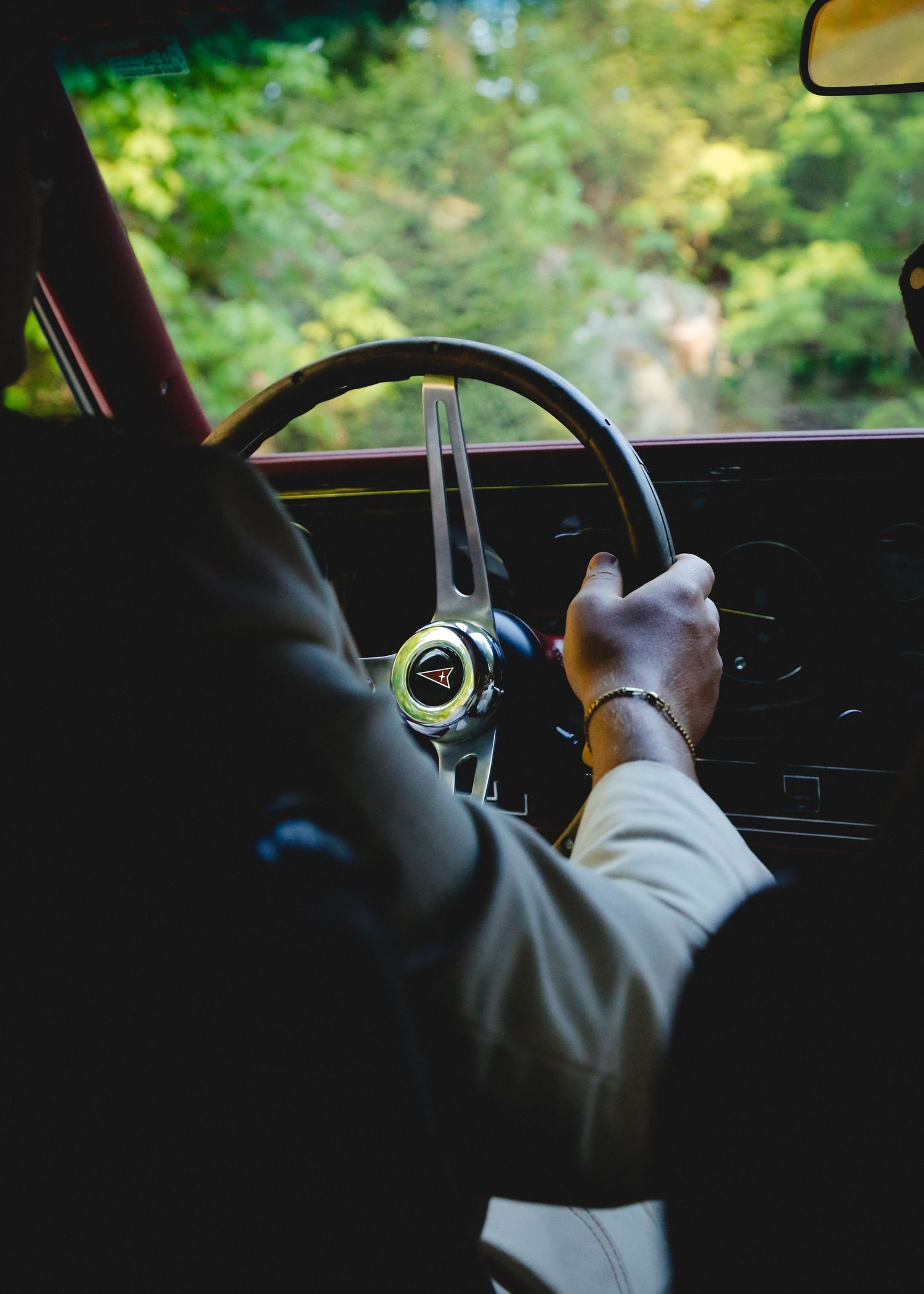 Close-up view of hands on a vintage steering wheel while driving through lush greenery.