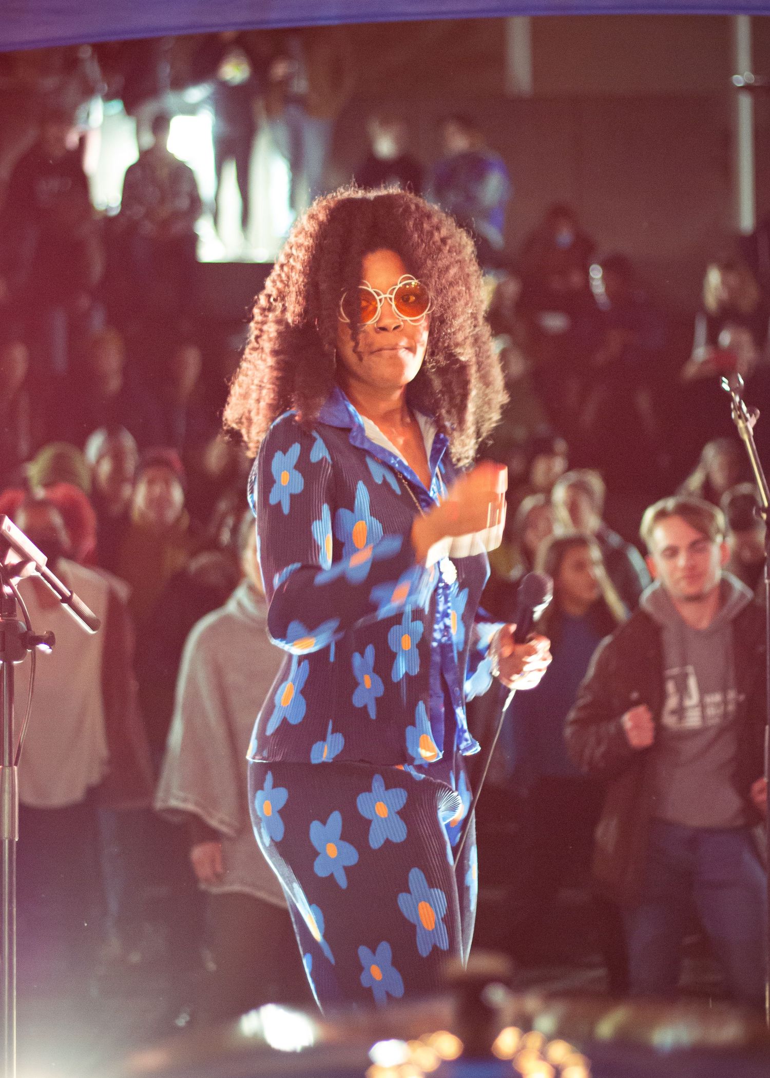 Performer in a blue floral dress on stage under theatrical lighting.