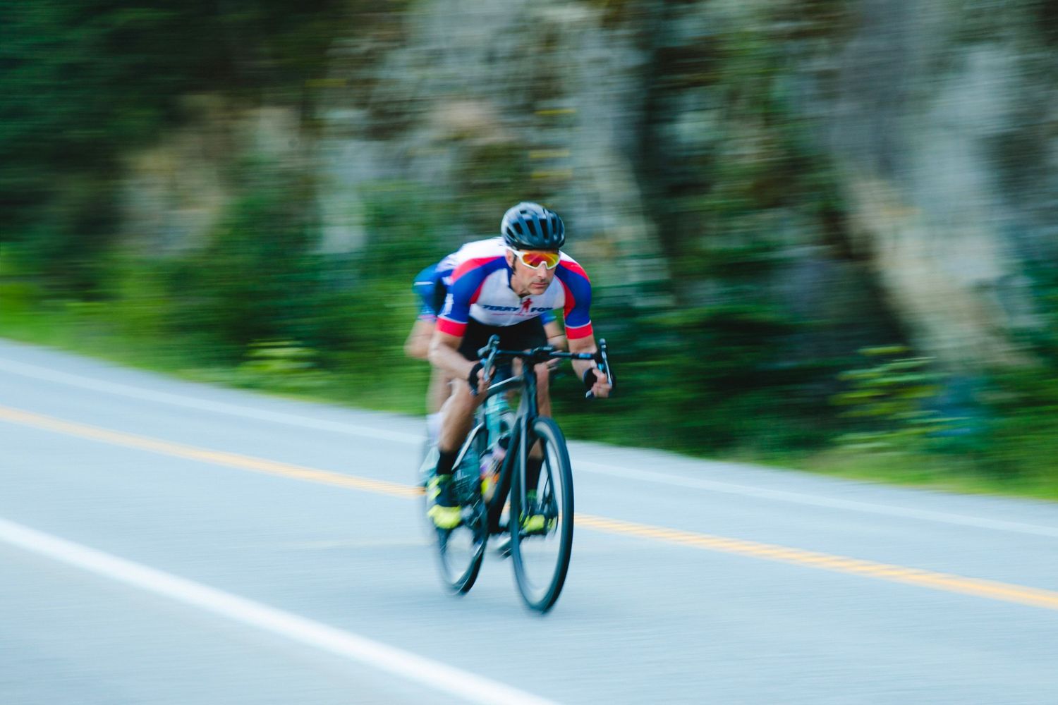 Cyclist in blue jersey races down road with motion blur effect.