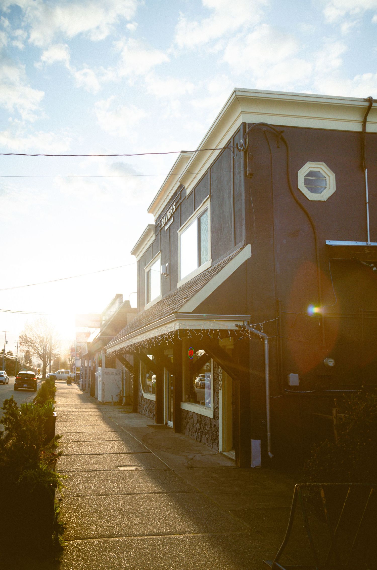 Small town storefront building with sun flare on a sidewalk during sunset creating a warm nostalgic atmosphere.