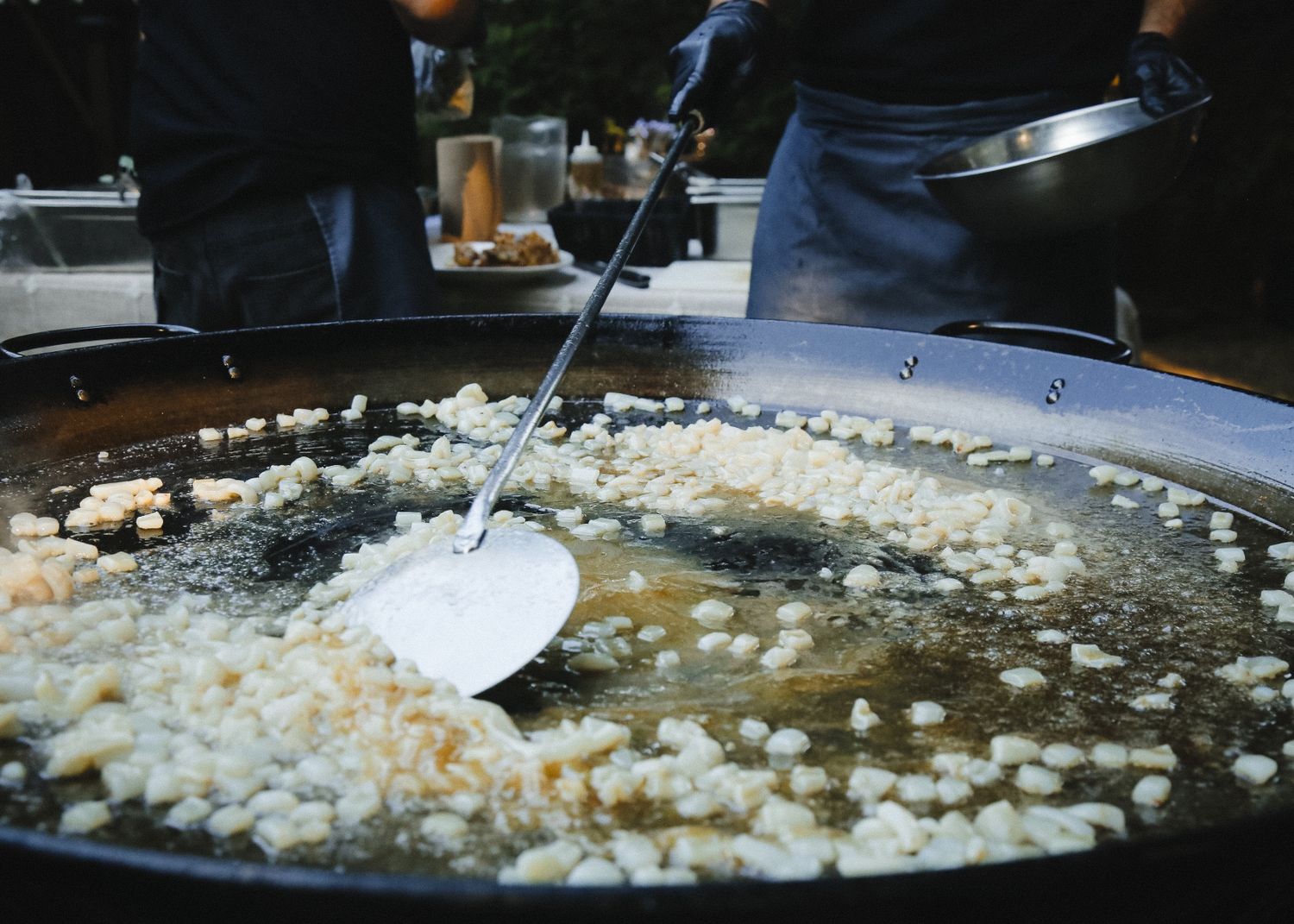 Large paella pan being stirred during outdoor cooking event.
