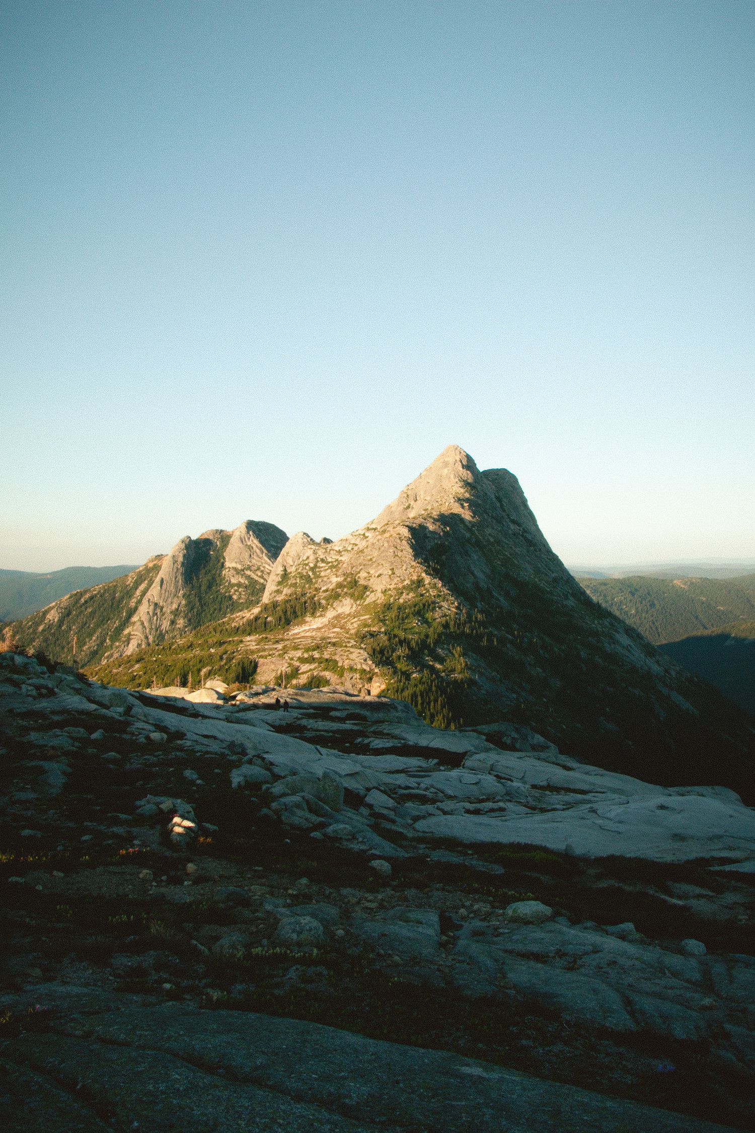 Rocky mountain peak against clear blue sky in golden evening light.