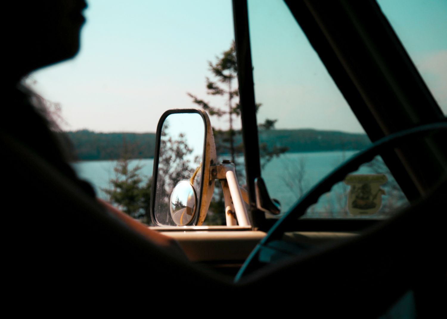 View through a car windshield of a scenic lake and forest landscape.