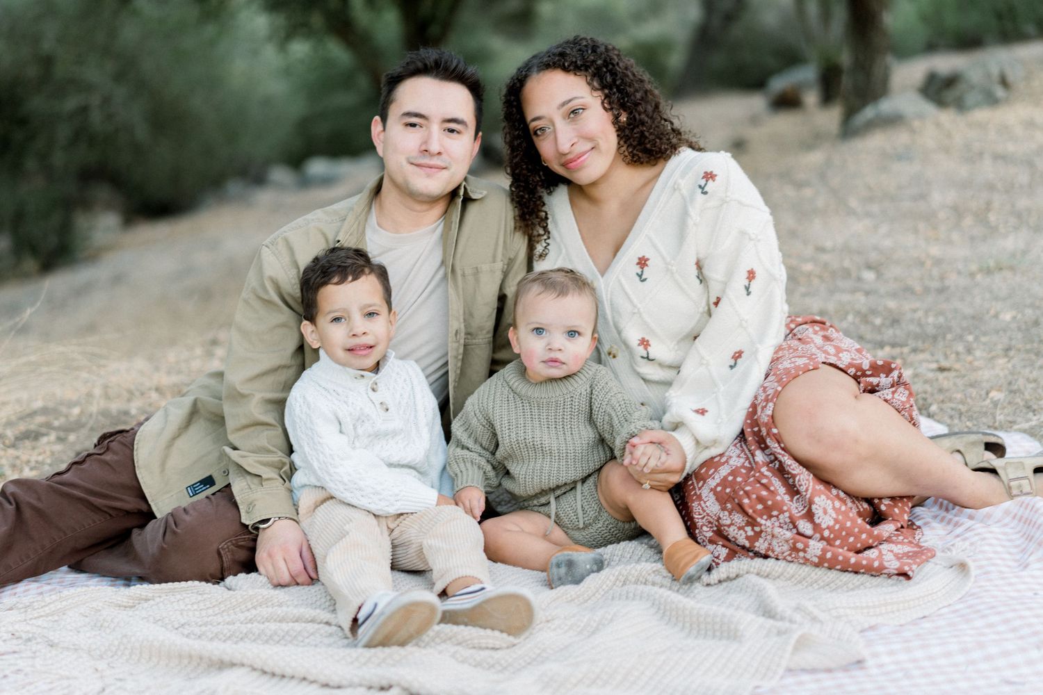 Family of four sits together on blanket for outdoor portrait session.
