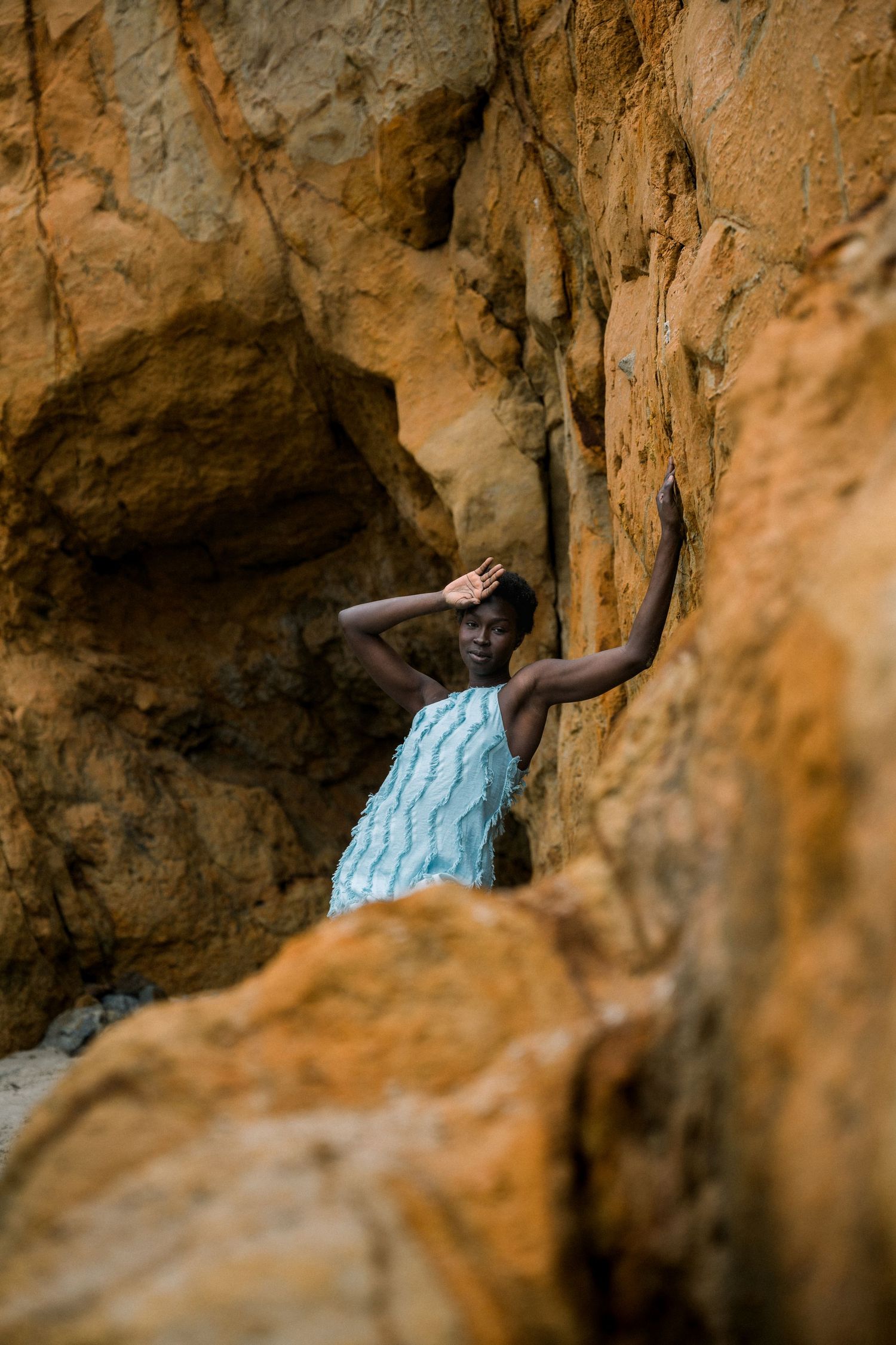 Person in light blue dress poses expressively among rocky cave formations.