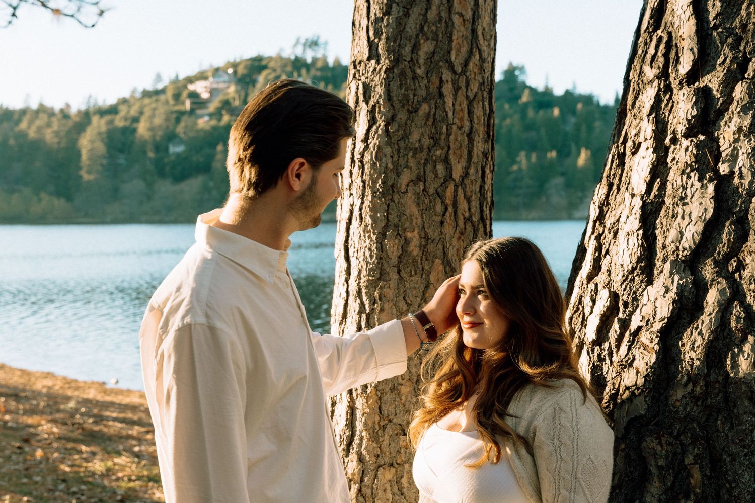 Intimate embrace between couple by large tree with lake in background.
