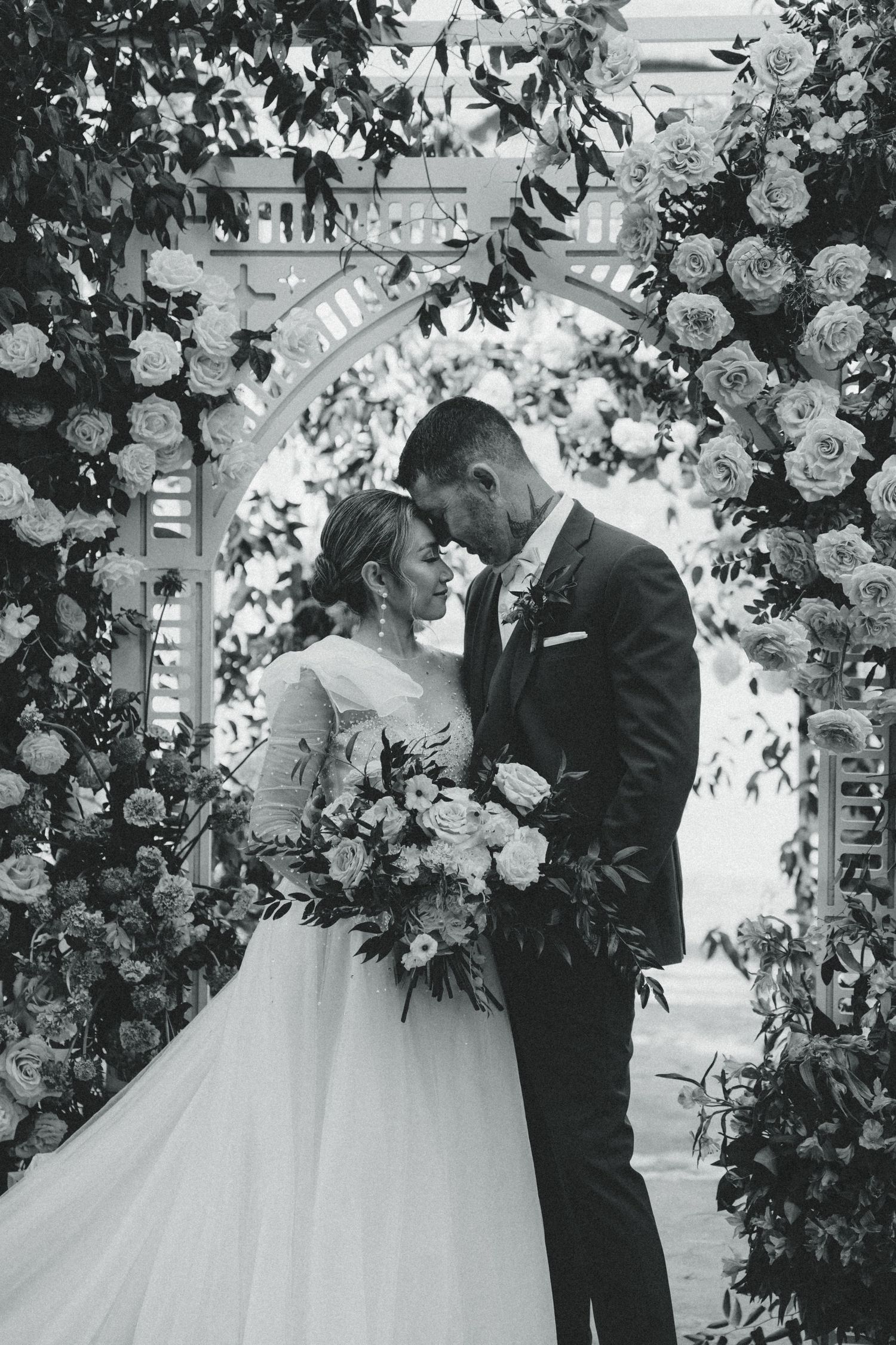 A romantic moment under a floral arch decorated with roses and greenery.
