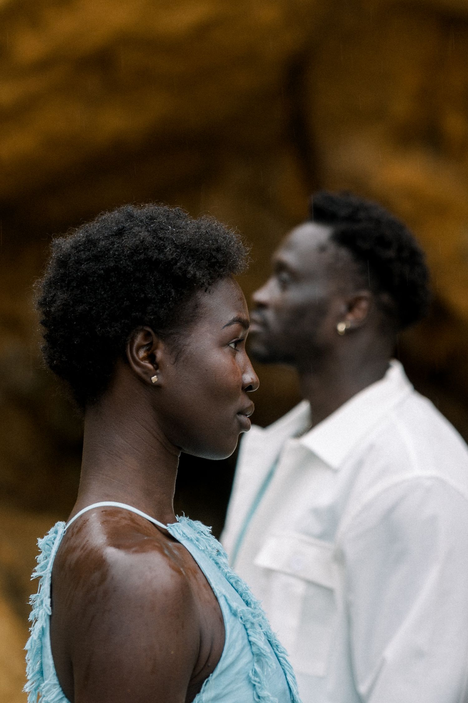 Dramatic profile shot of couple in complementary white and turquoise attire against cave wall.