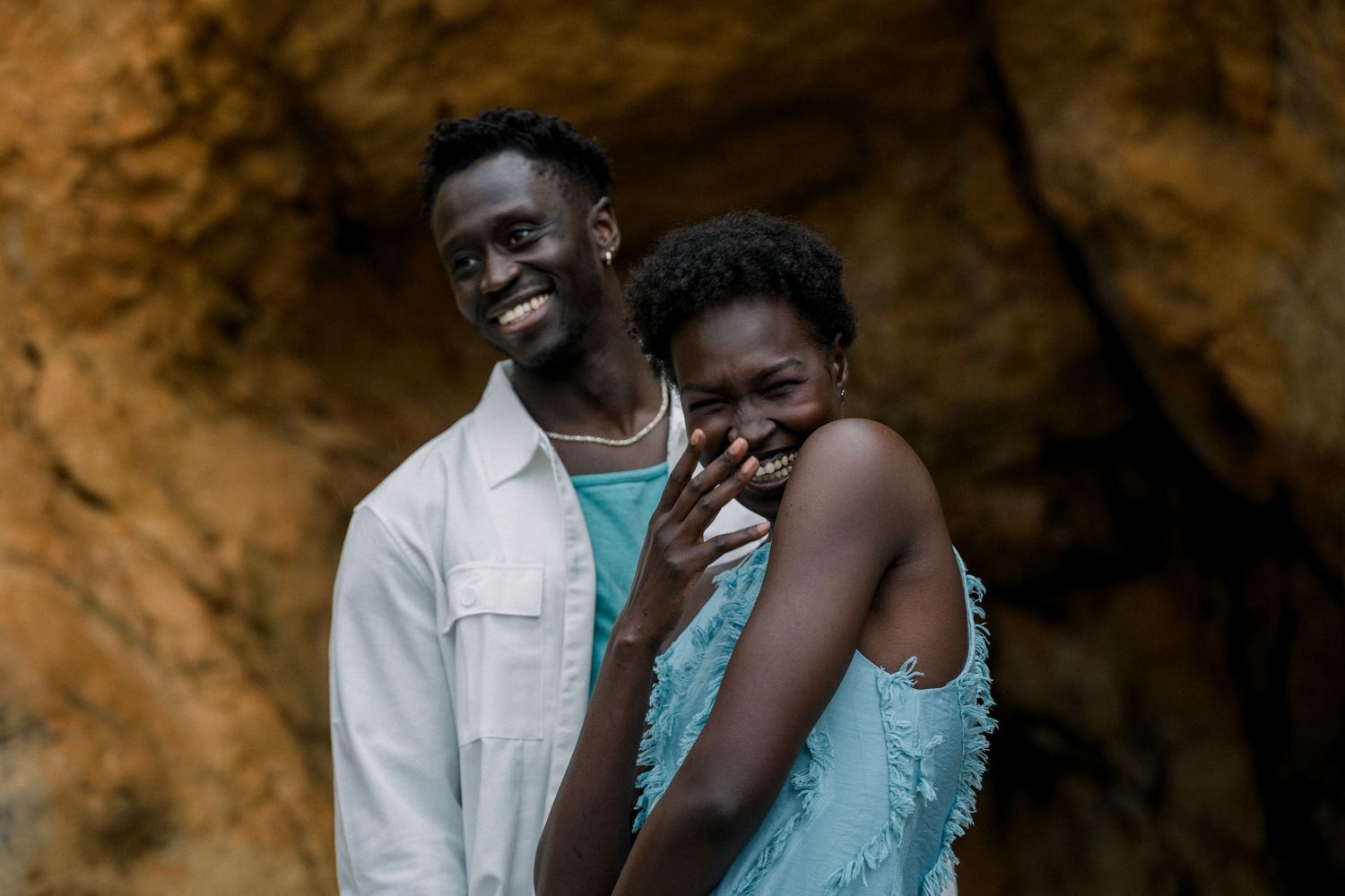 A romantic couple shares a tender moment while standing in front of a cave entrance.