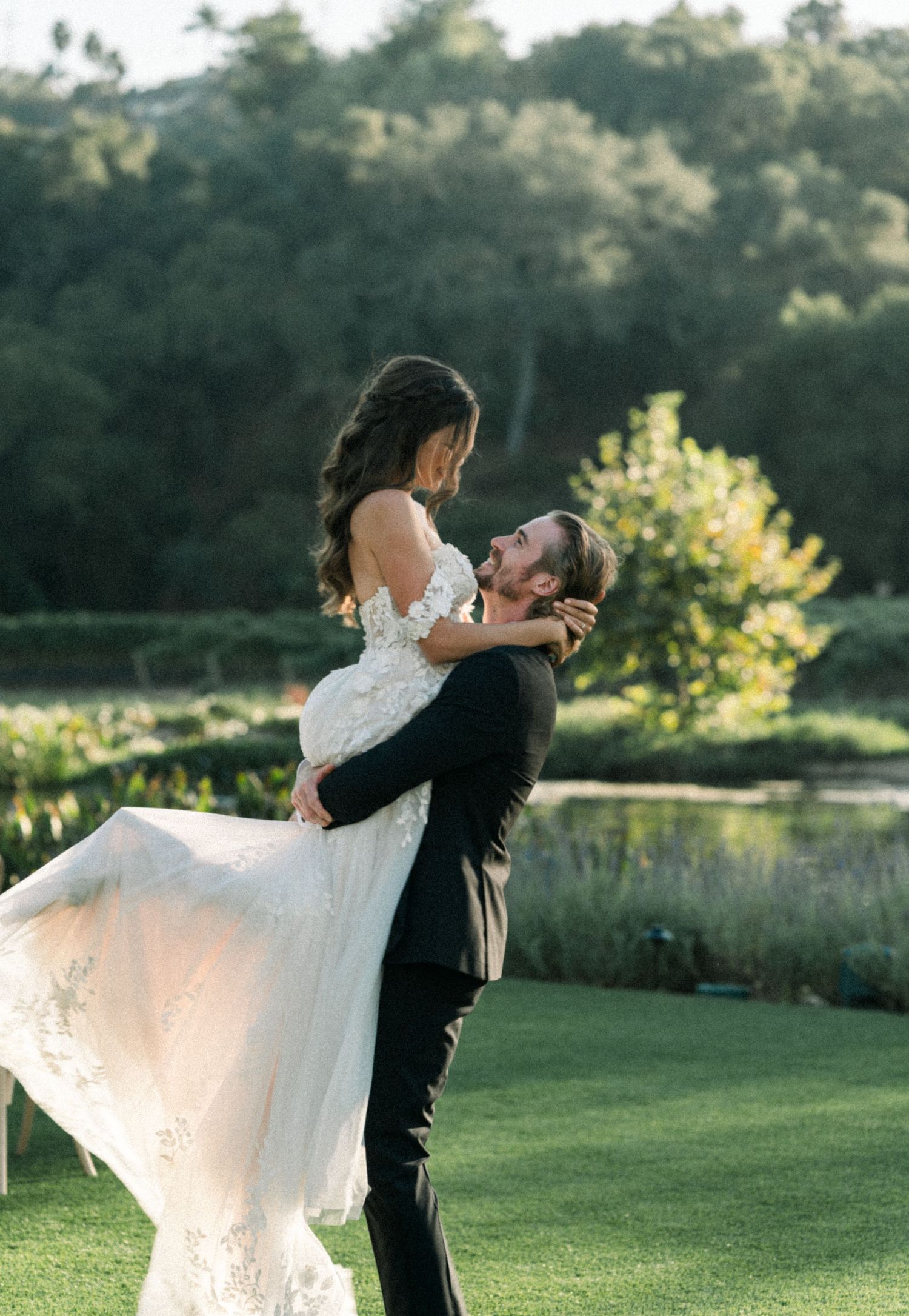 Joyful wedding couple embracing on manicured lawn during golden hour.