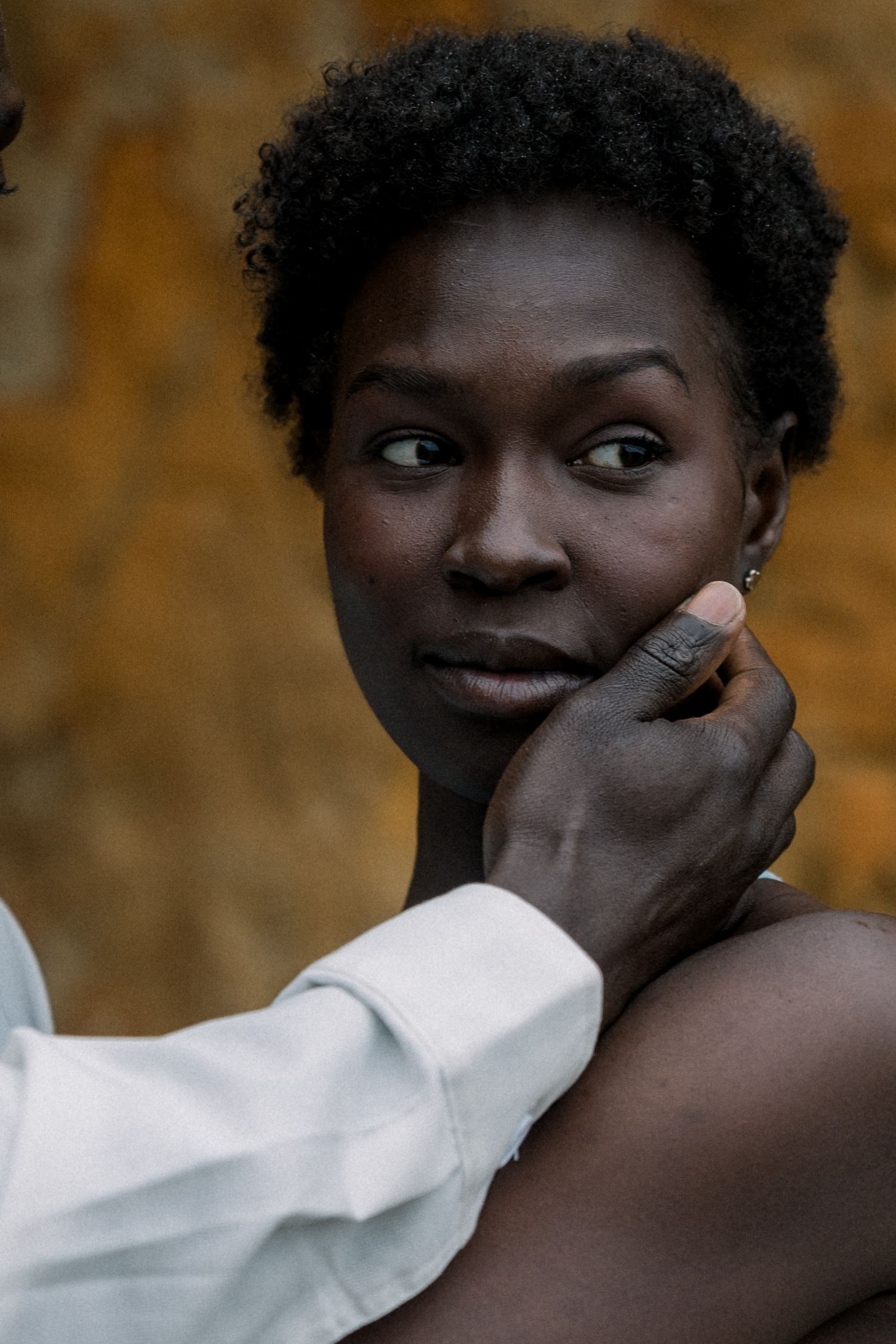 Intimate close-up portrait with gentle hand gesture against warm-toned rocky background.