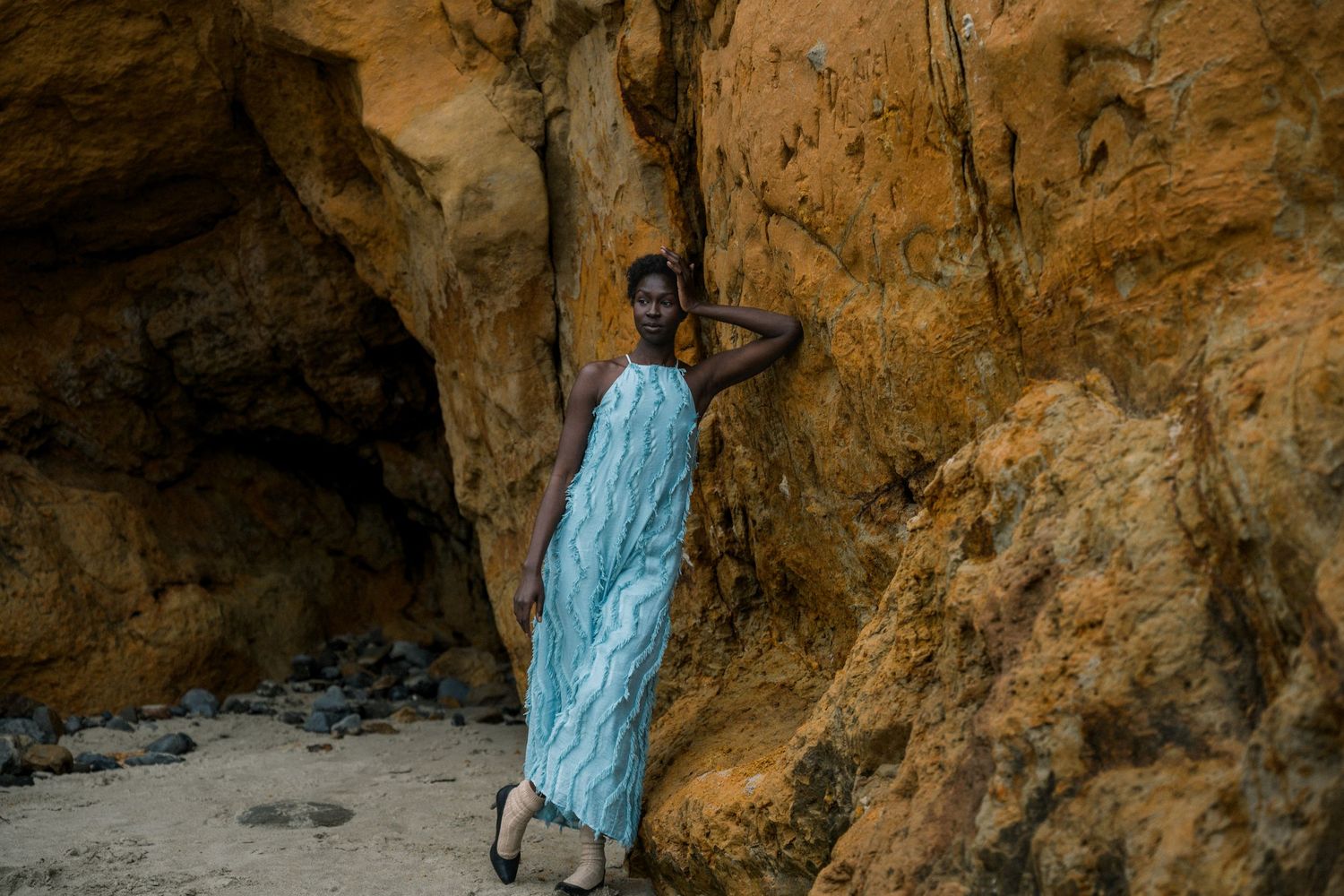 Figure in blue dress stands gracefully against dramatic cave rock formations.