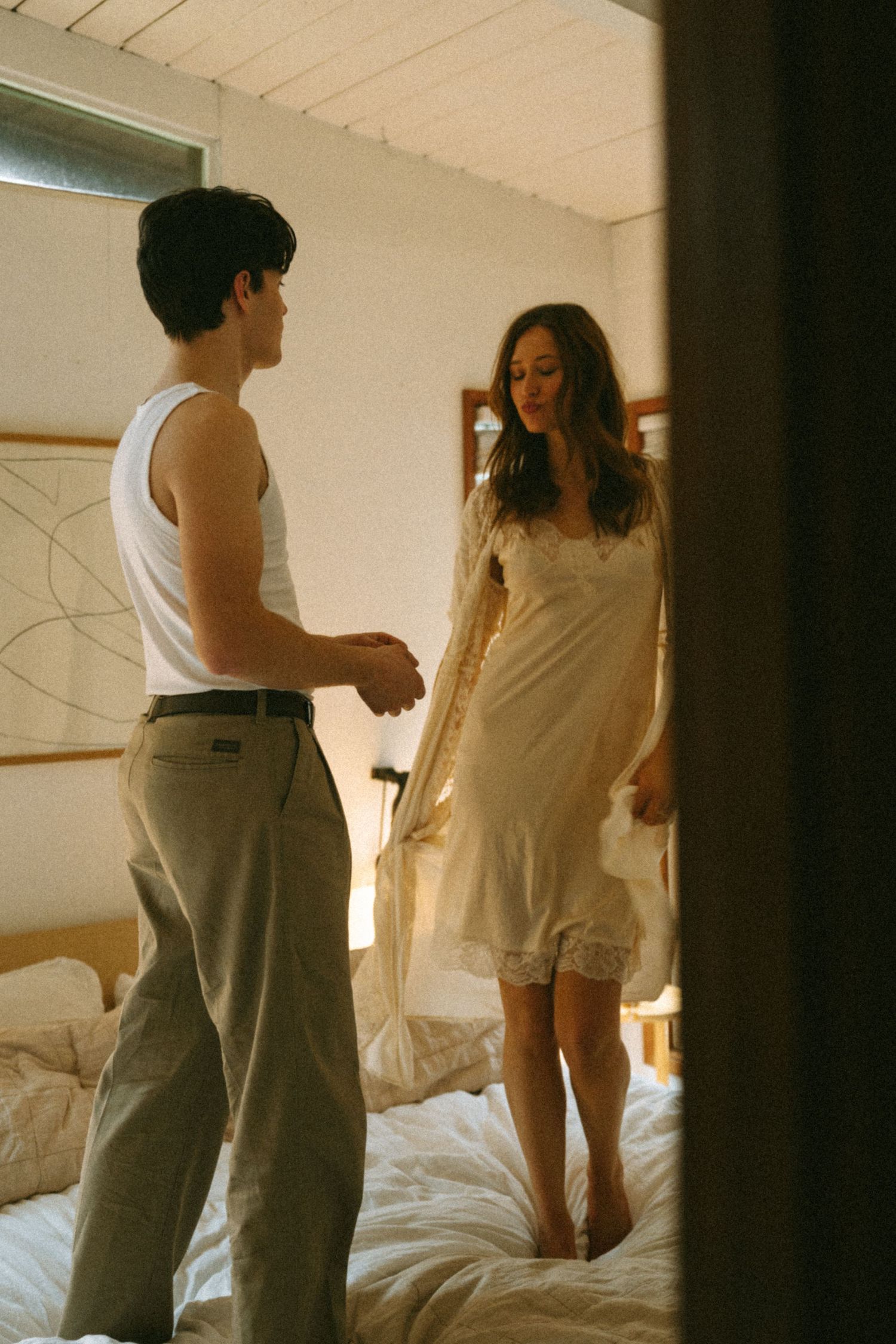 Candid indoor scene of couple sharing playful moment on bed in sunlit room.