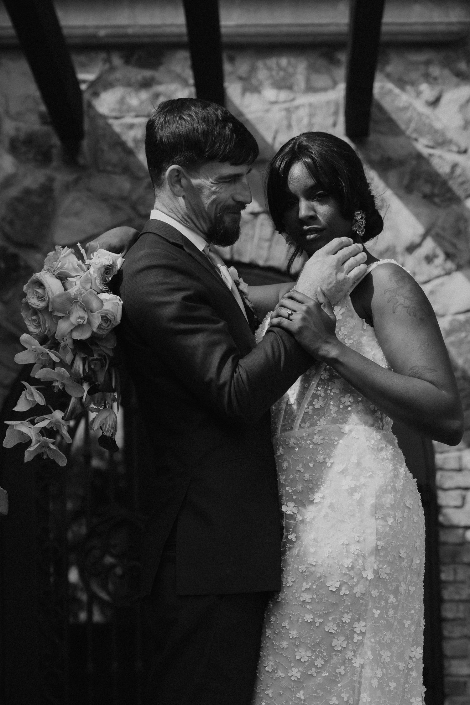An intimate black and white wedding portrait against a stone wall backdrop.