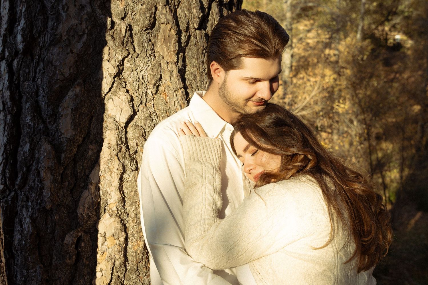 Romantic sunlit moment between couple near tree trunk in natural setting.
