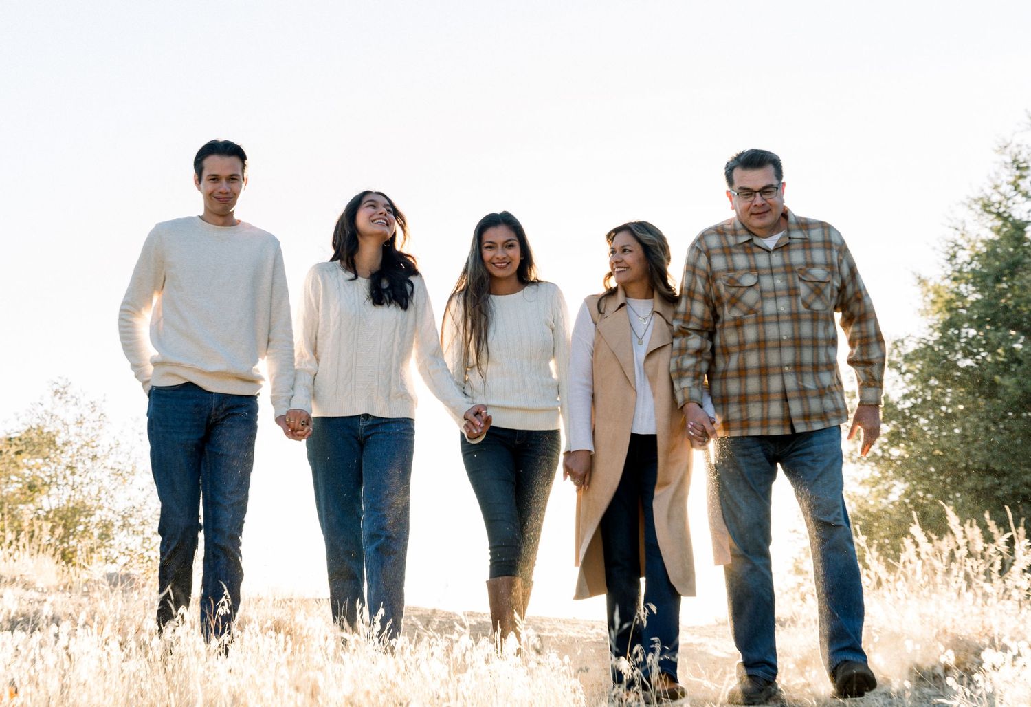 Family of five wearing coordinated neutral outfits poses together in sunlit field.