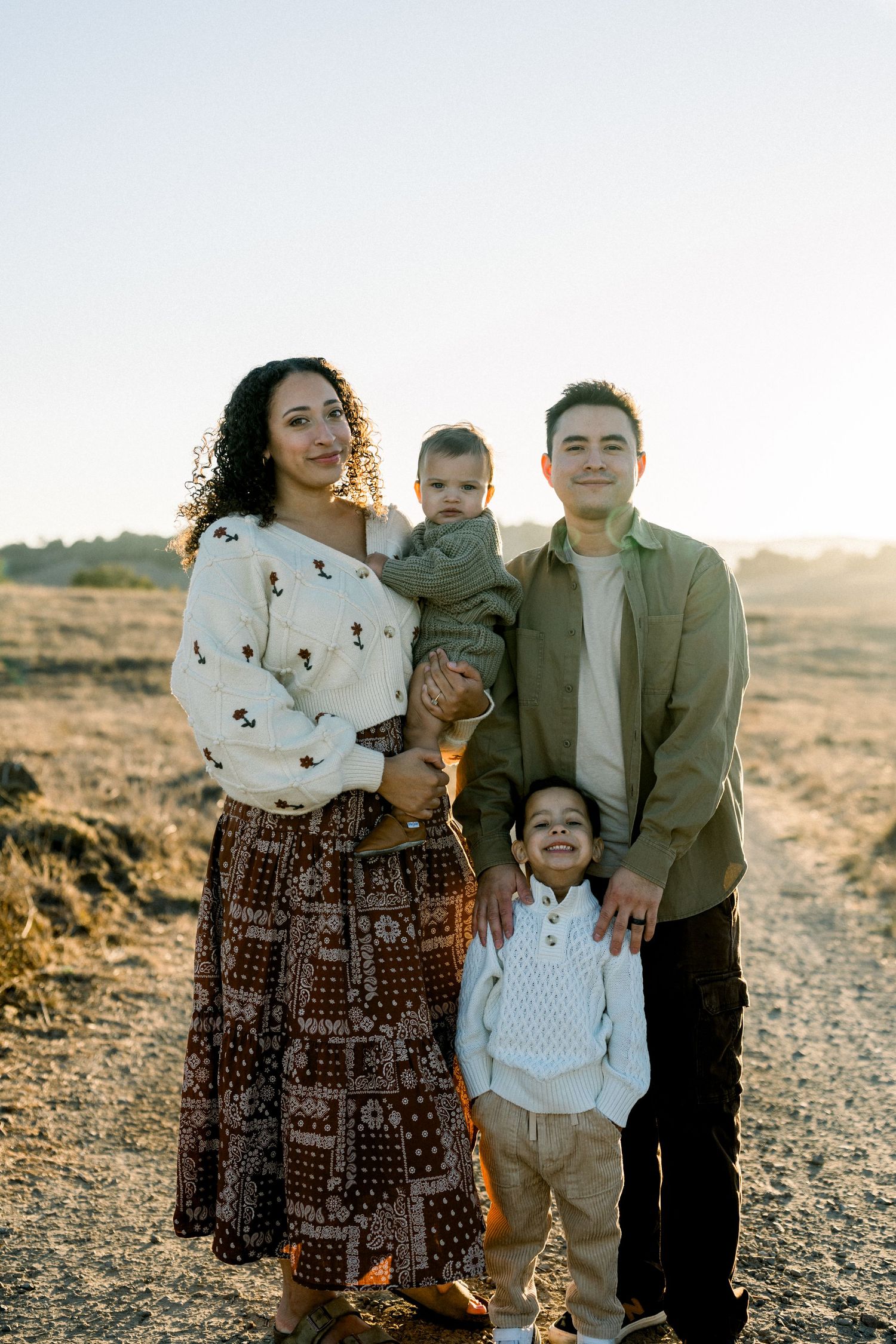 A family of four poses together at sunset on a desert trail wearing casual attire.