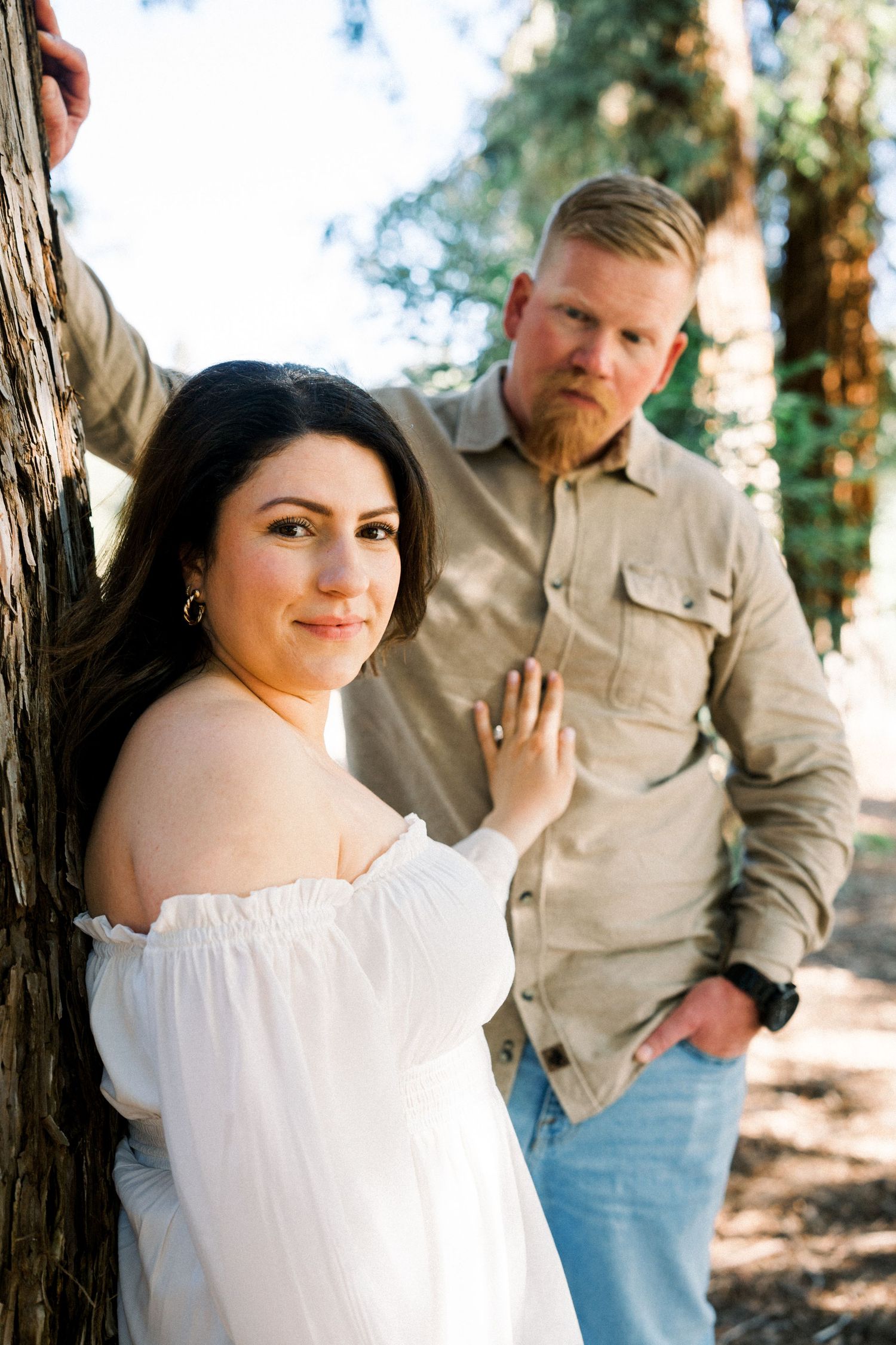 Intimate outdoor portrait of couple leaning against tree trunk in natural lighting.