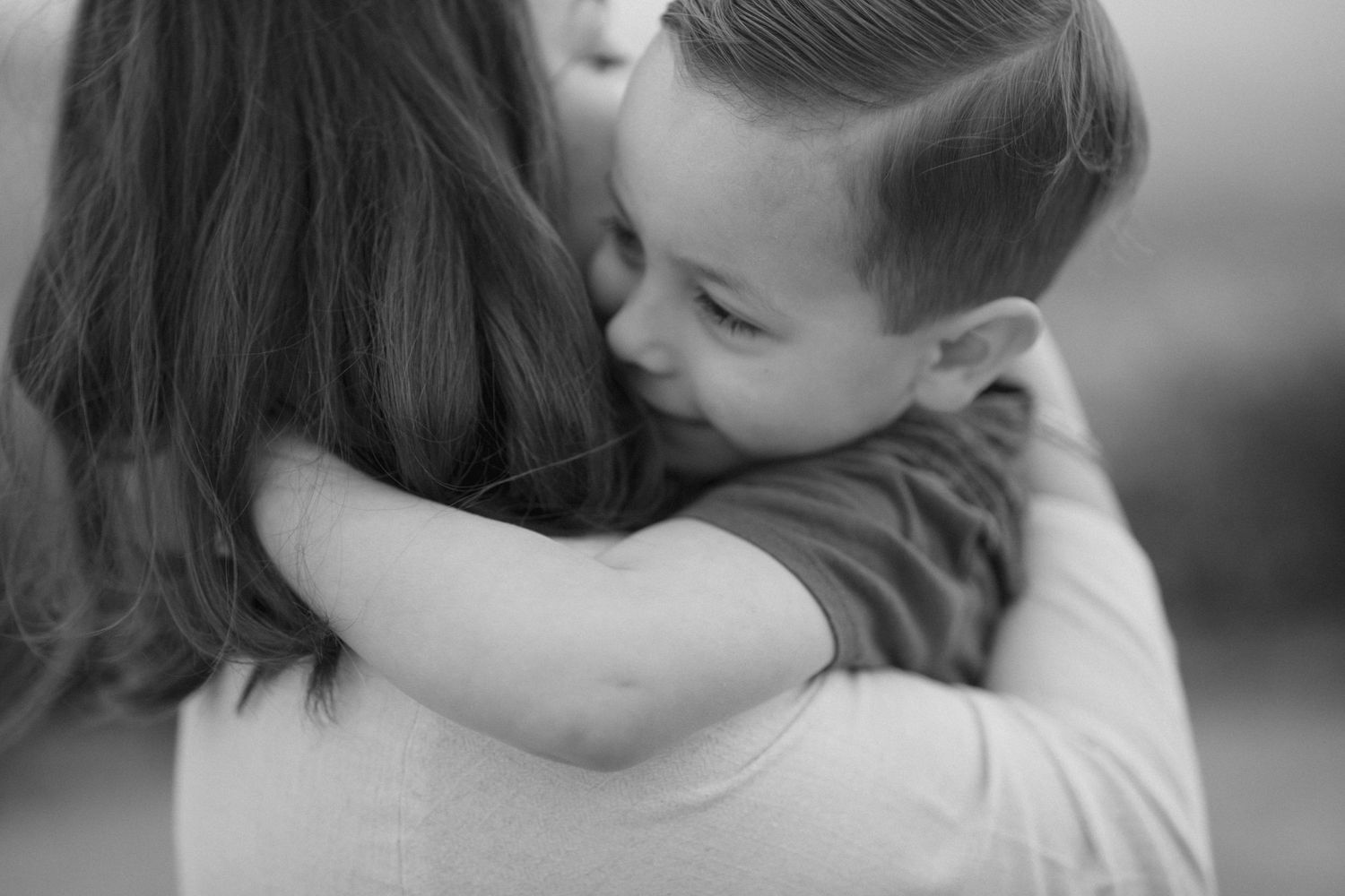 A tender black and white portrait showing a child and parent sharing a loving embrace.