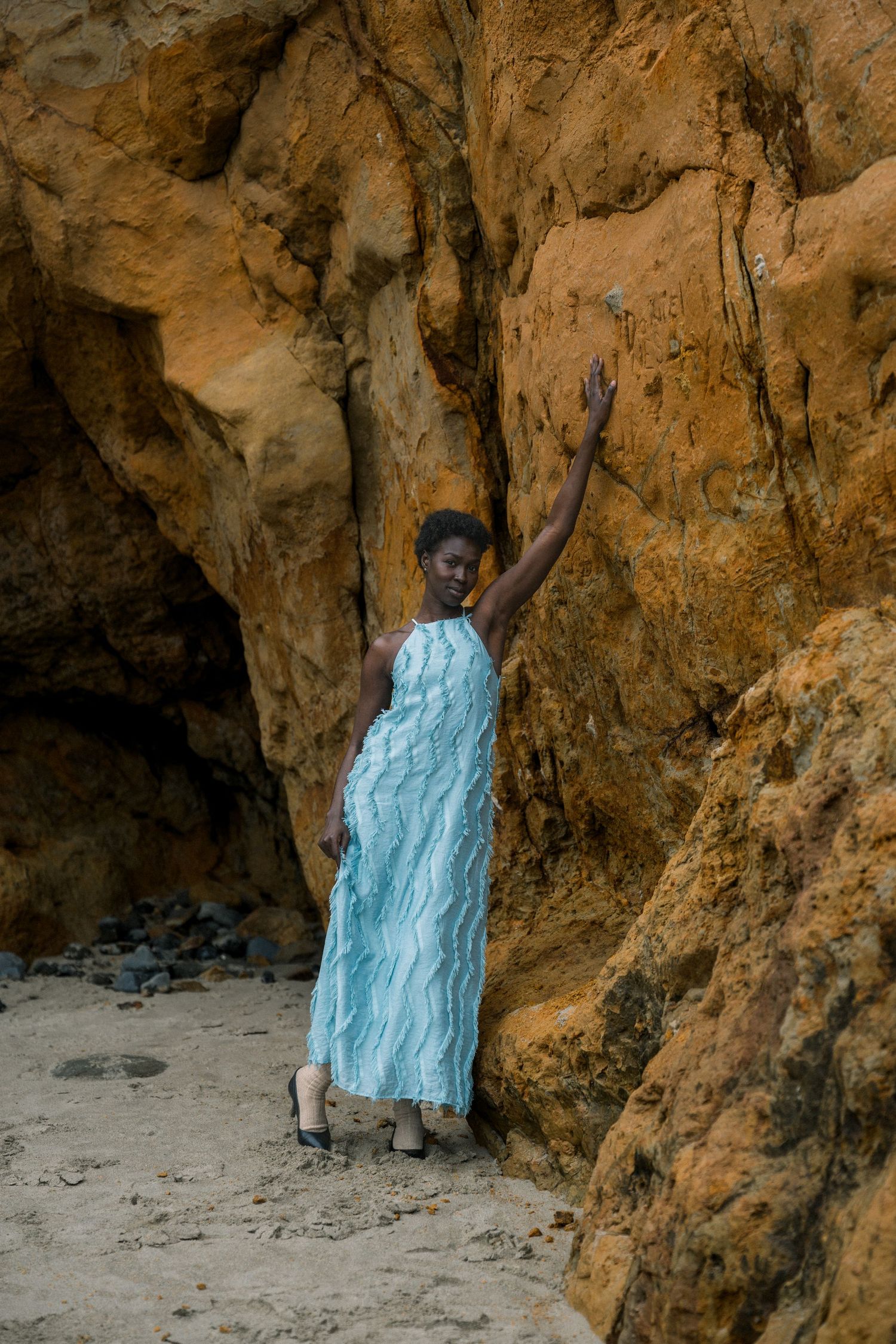 Person in flowing turquoise dress poses dramatically against textured cave walls.