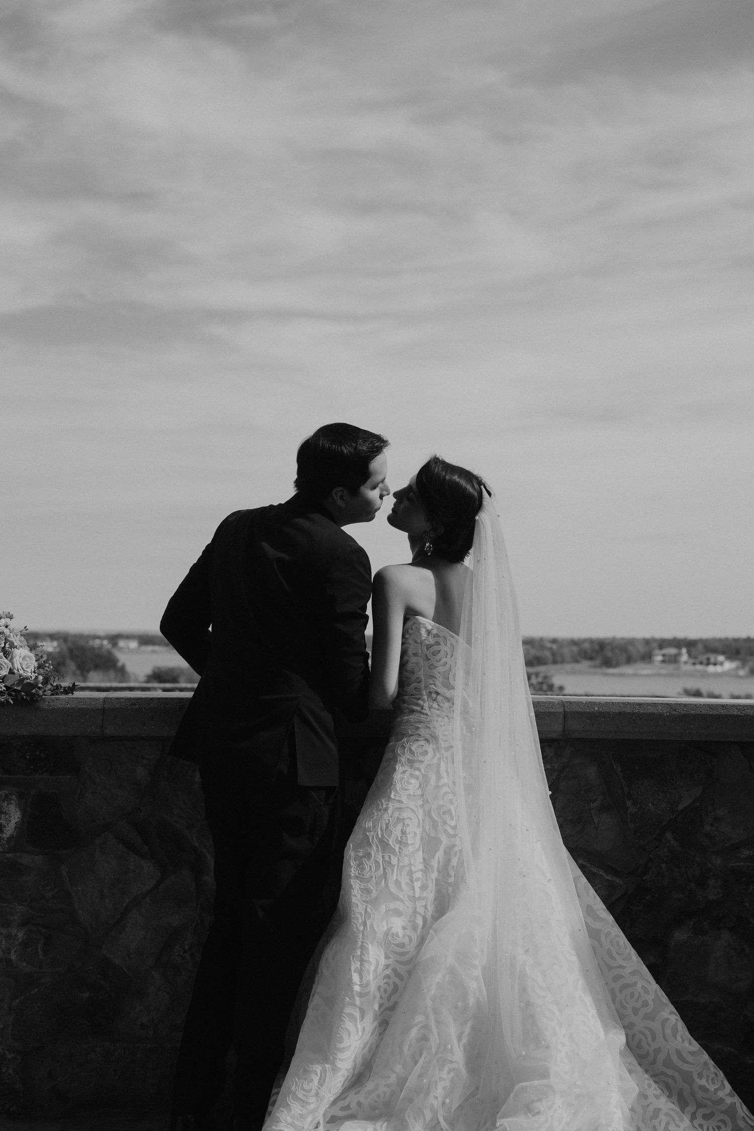 Silhouette of newlyweds in formal attire overlooking a scenic landscape at sunset.