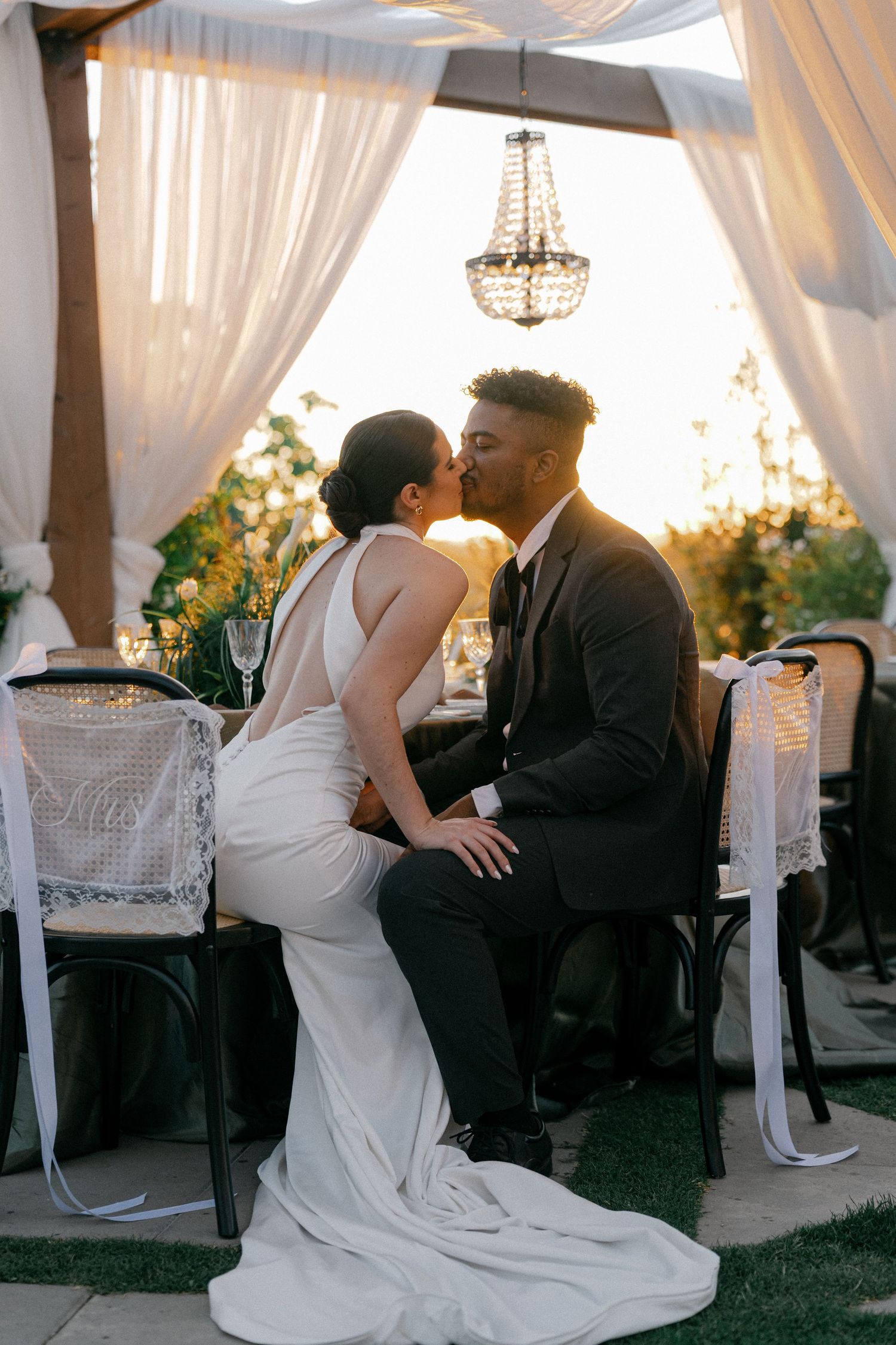 Elegant wedding couple shares intimate moments in a draped tent with crystal chandeliers and white decor.