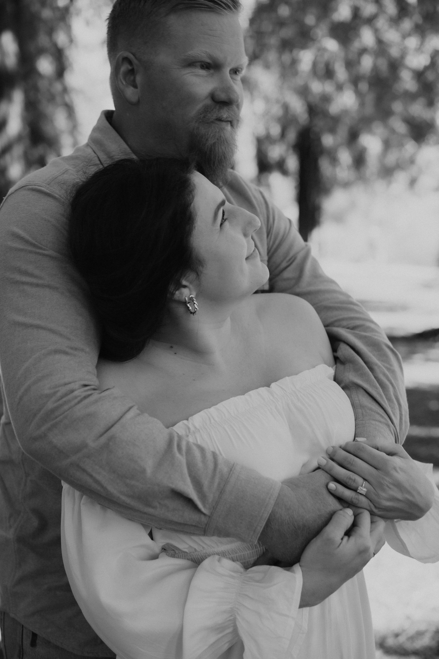 Romantic black and white portrait of a couple embracing outdoors with soft natural lighting.