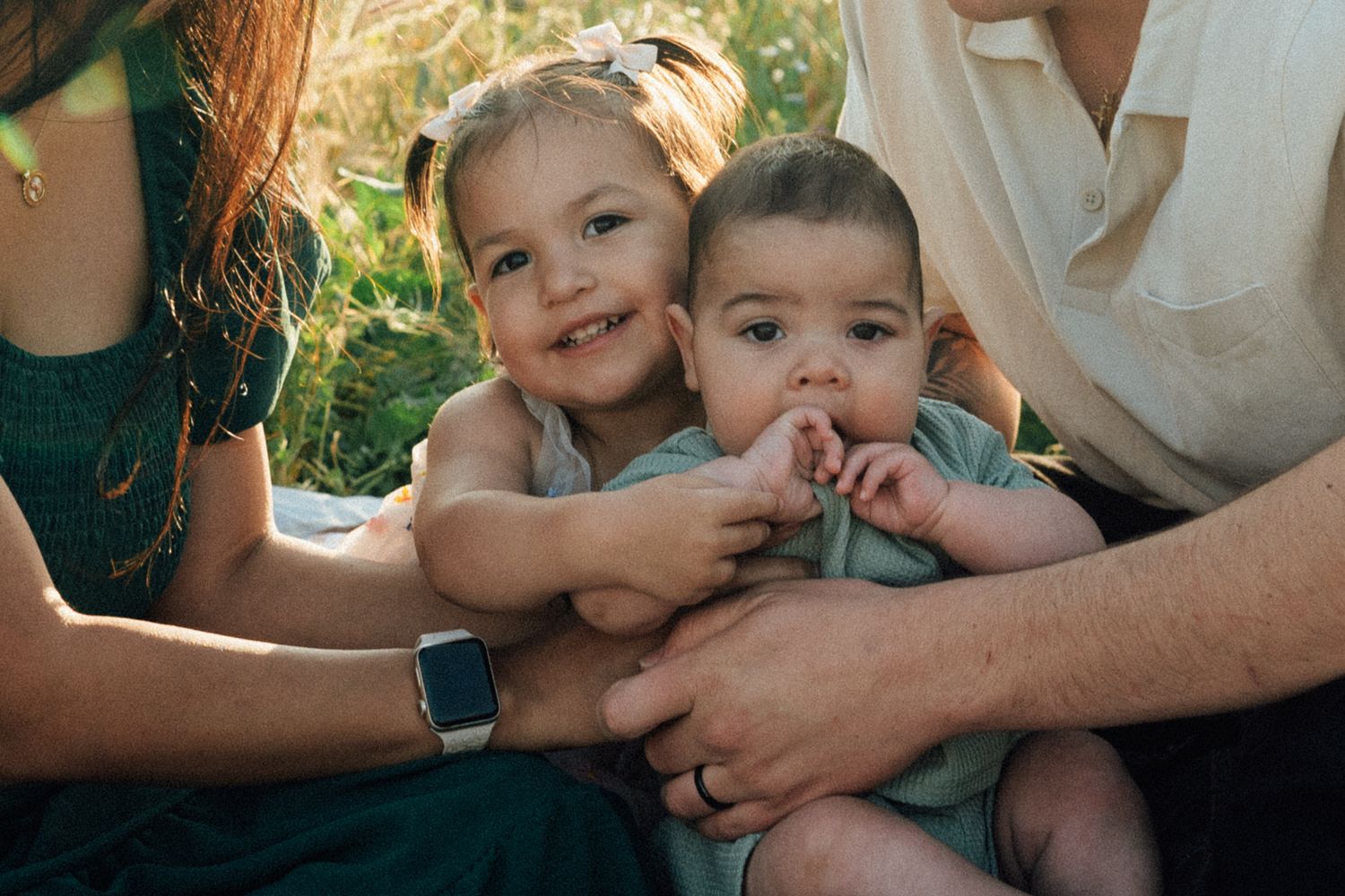 Family candid moment showing children with parents sitting together outdoors in natural sunlight.
