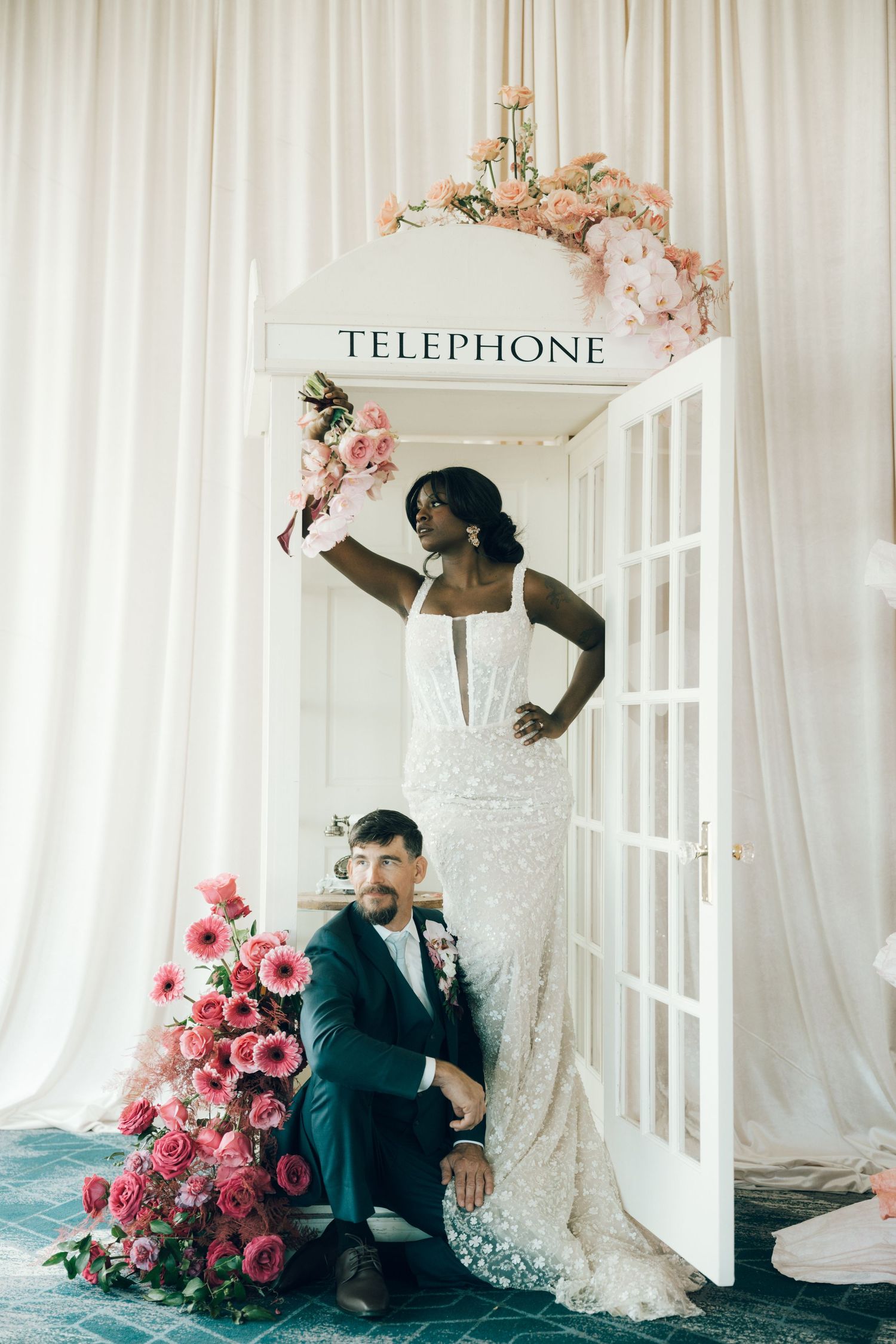 Romantic wedding photoshoot with vintage telephone booth prop and pink rose arrangements.