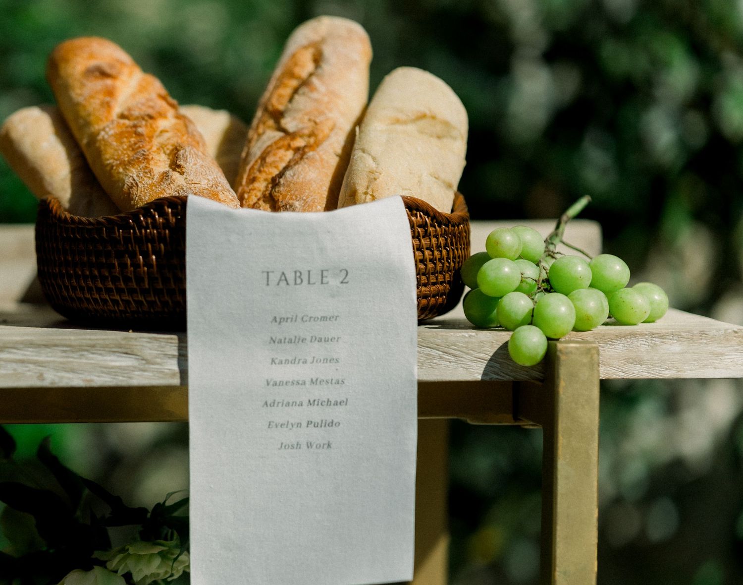 Fresh bread basket with menu card and green grapes on rustic wooden surface.