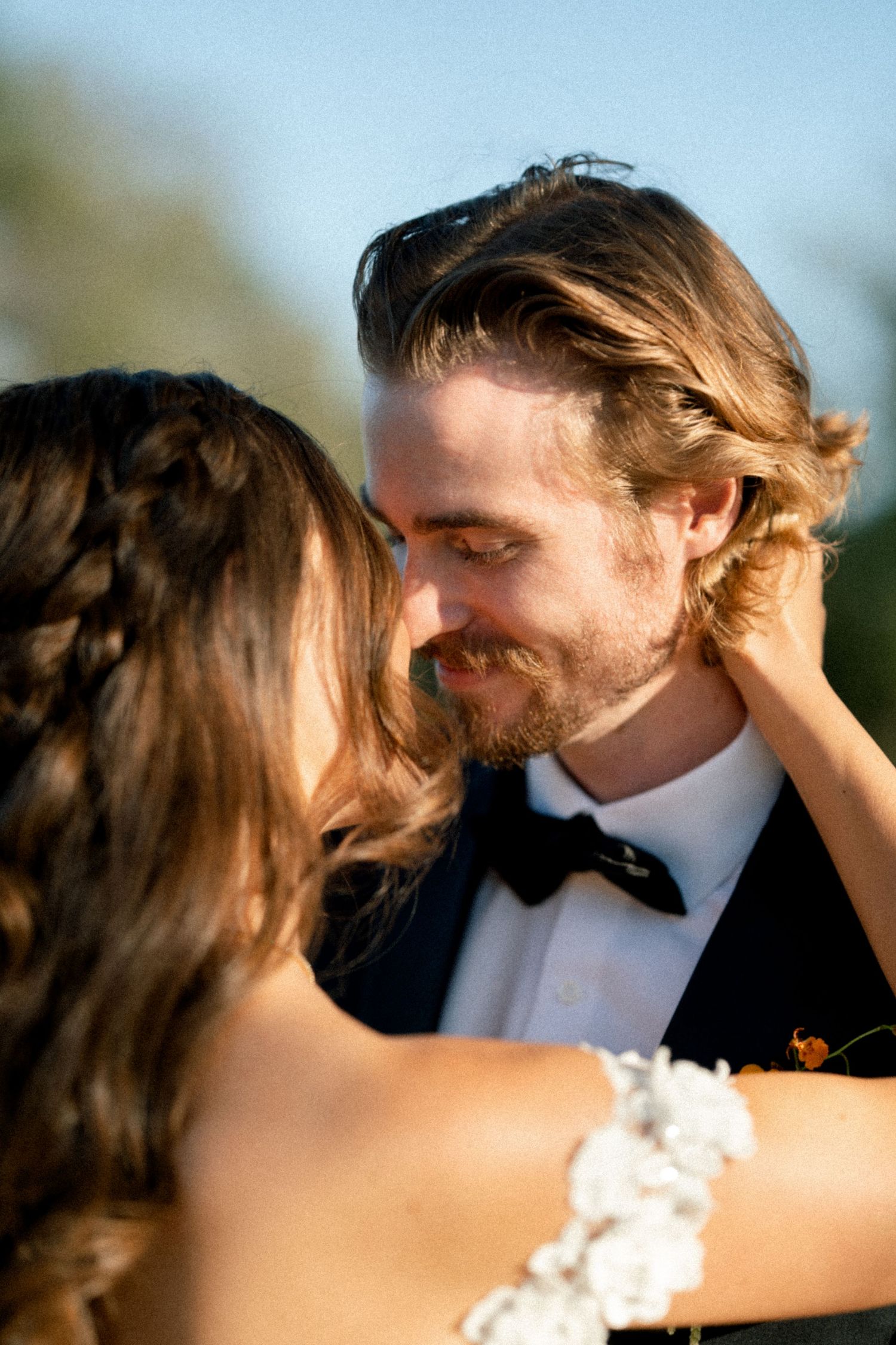Romantic outdoor moment between newlyweds in formal attire at sunset.