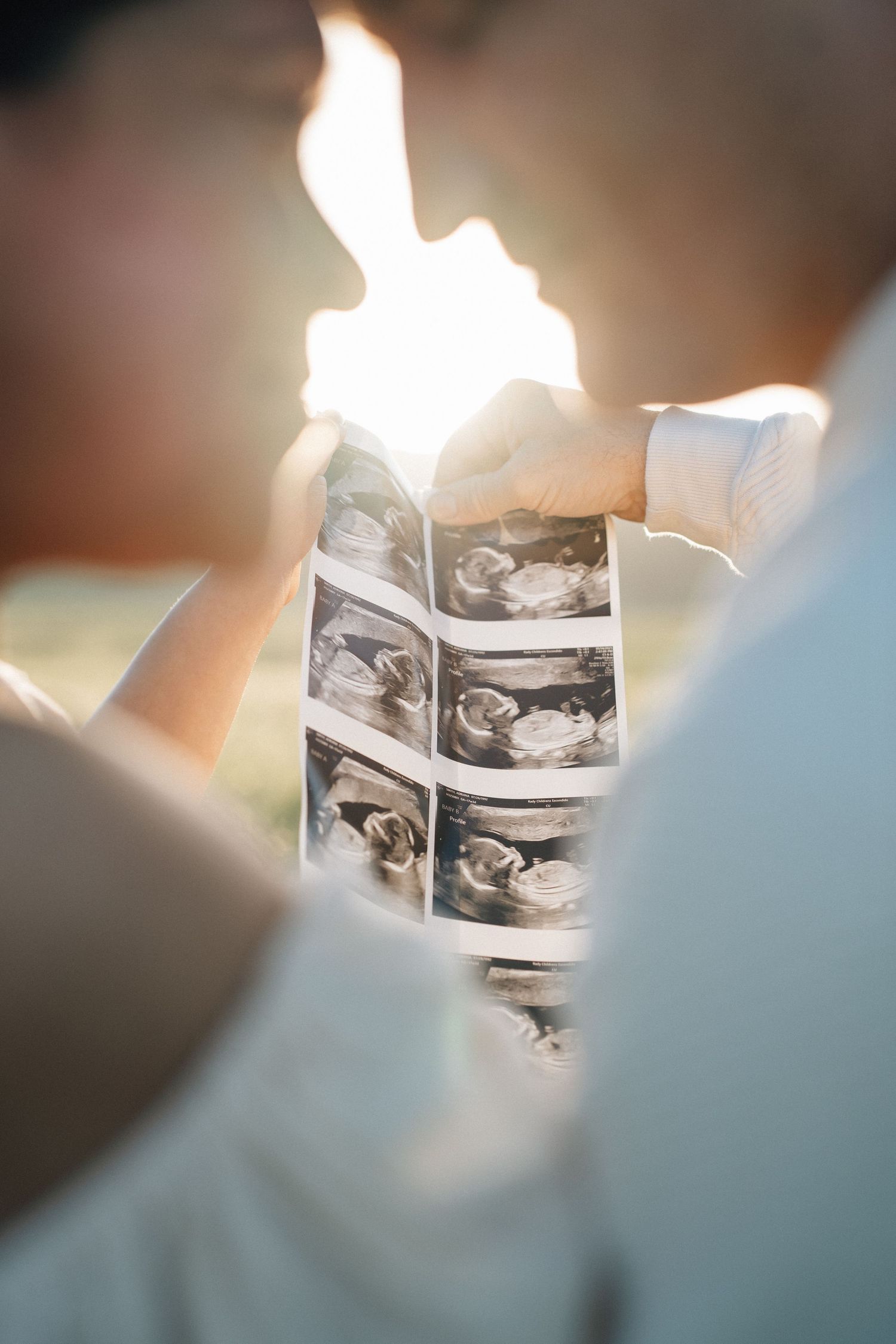 Close-up view of hands holding black and white ultrasound images with sunlight filtering through.