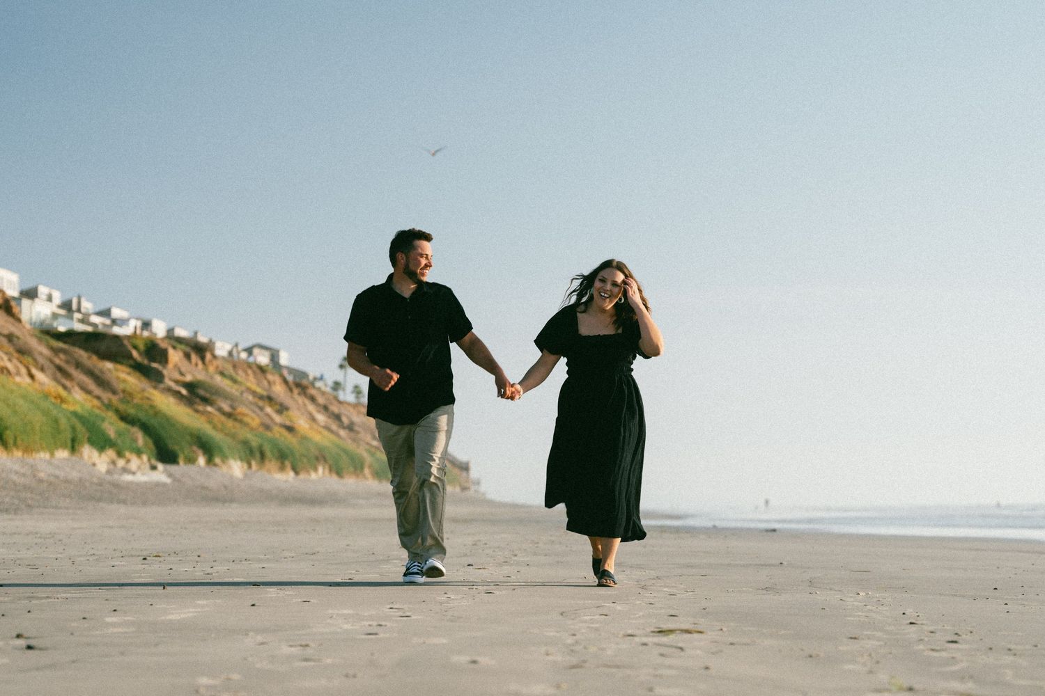 Couple walking hand in hand along scenic coastal beach.