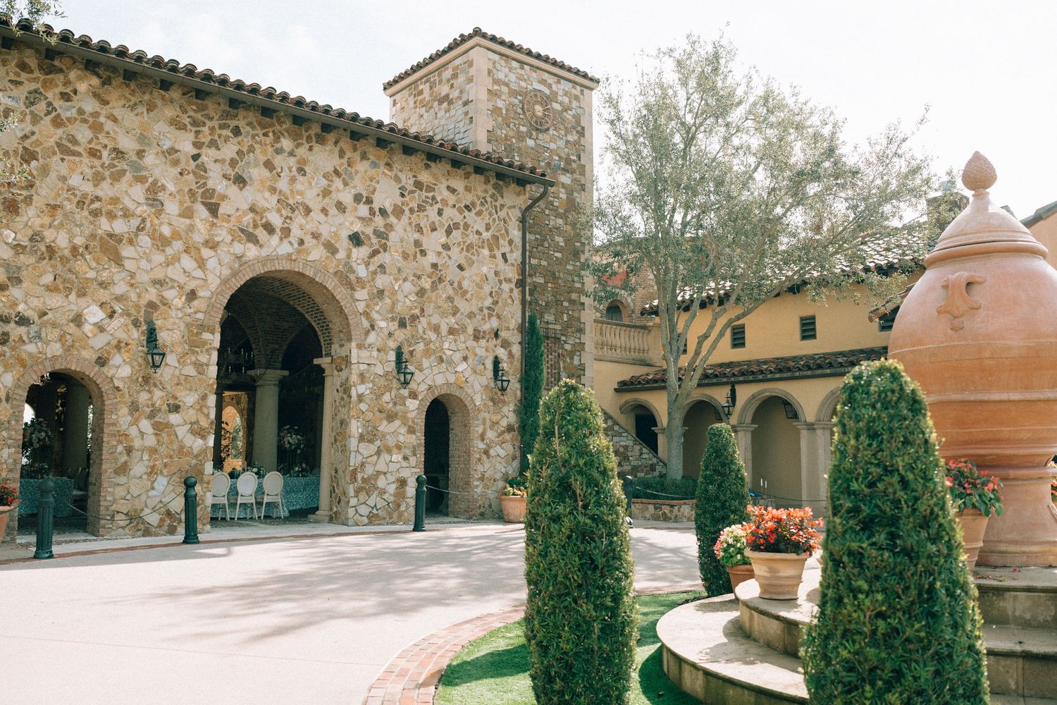 Mediterranean stone courtyard with arched entryway, cypress trees, and large terracotta planter.