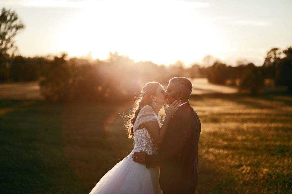 Romantica passeggiata al tramonto: gli sposi mano nella mano tra i campi, avvolti dalla magica luce della golden hour. Un'atmosfera calda e