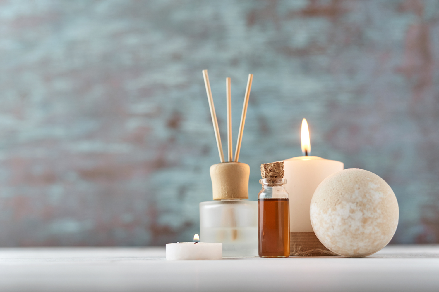 Aromatherapy spa items including diffuser, essential oils, and bath bomb on light surface.