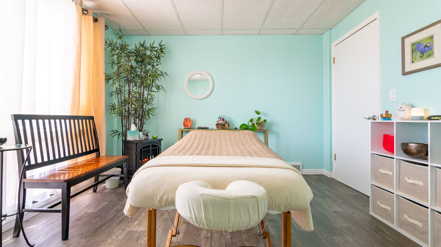Serene spa treatment room with massage table, bamboo plants and light teal walls.