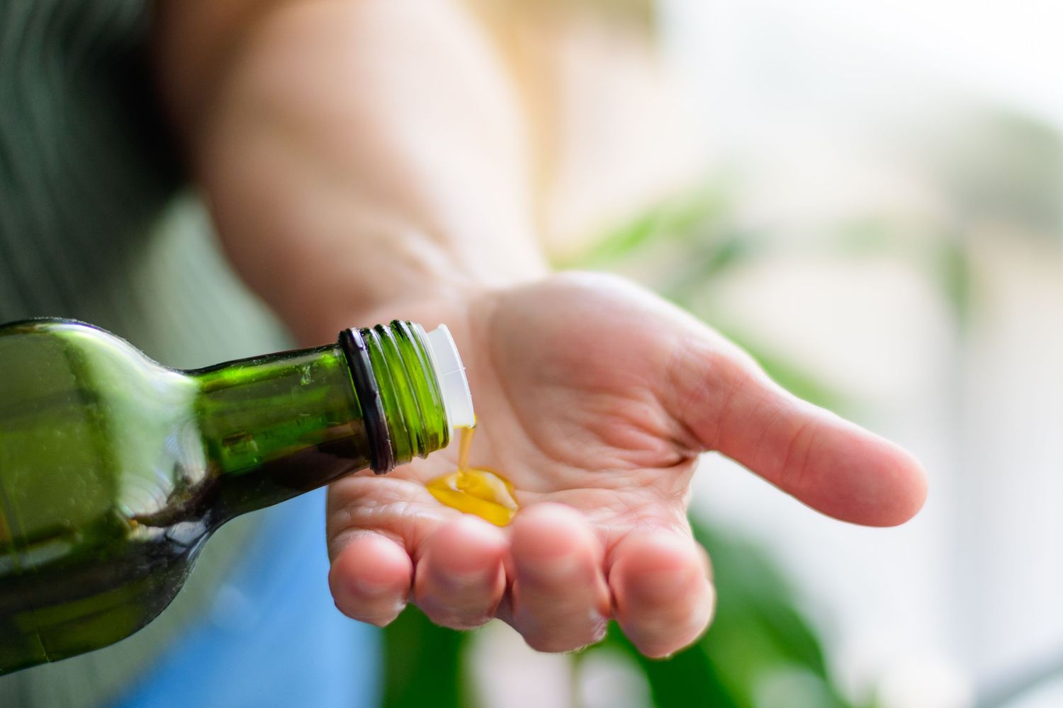 Hand pouring essential oil from a small green glass bottle.