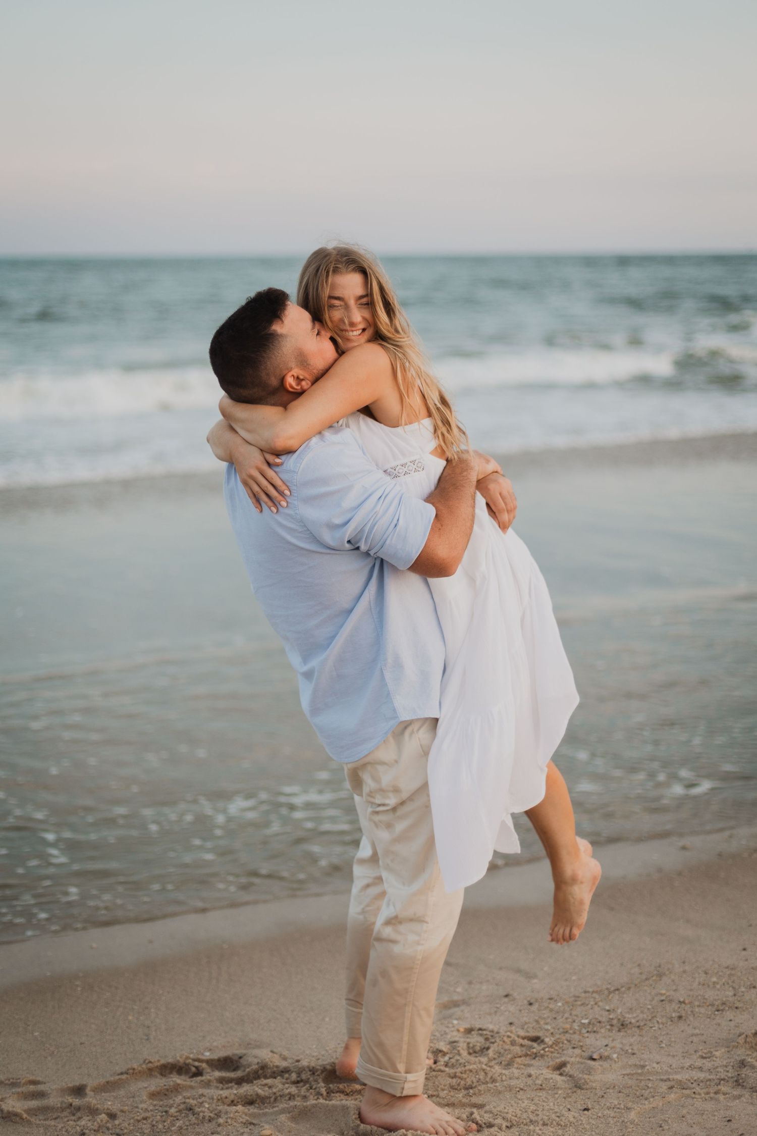 A couple shares an intimate moment on the beach at sunset with waves crashing behind them.
