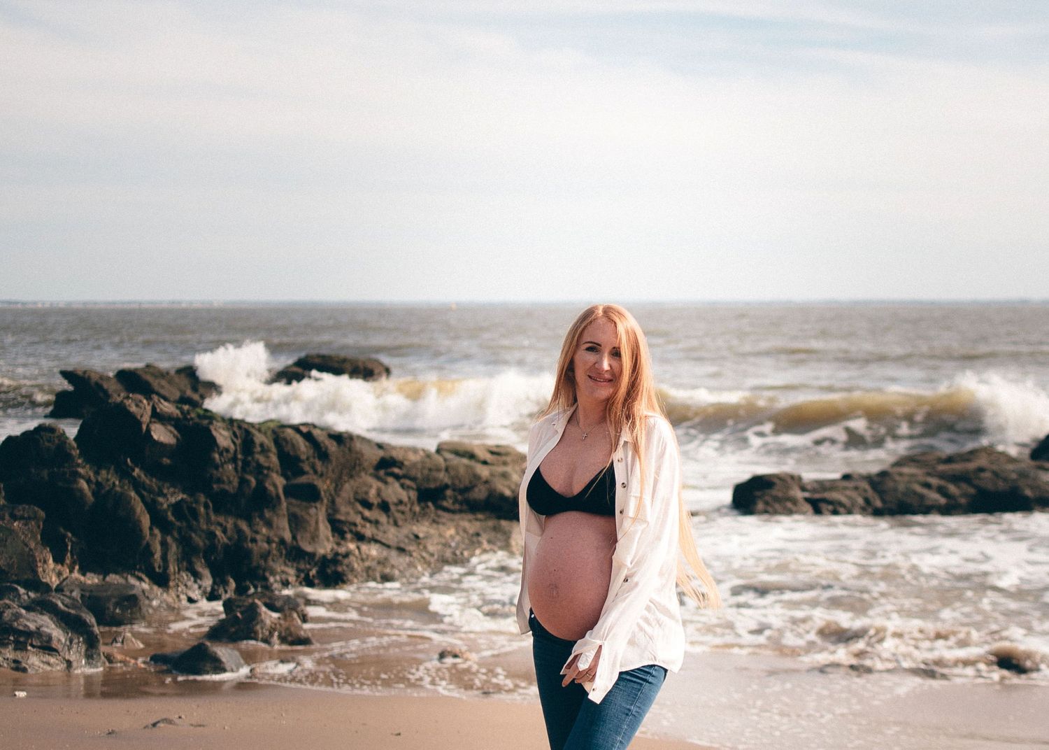 Femme enceinte debout sur la plage parmi les rochers, séance photo grossesse en lumière naturelle à Saint-Marc-sur-Mer