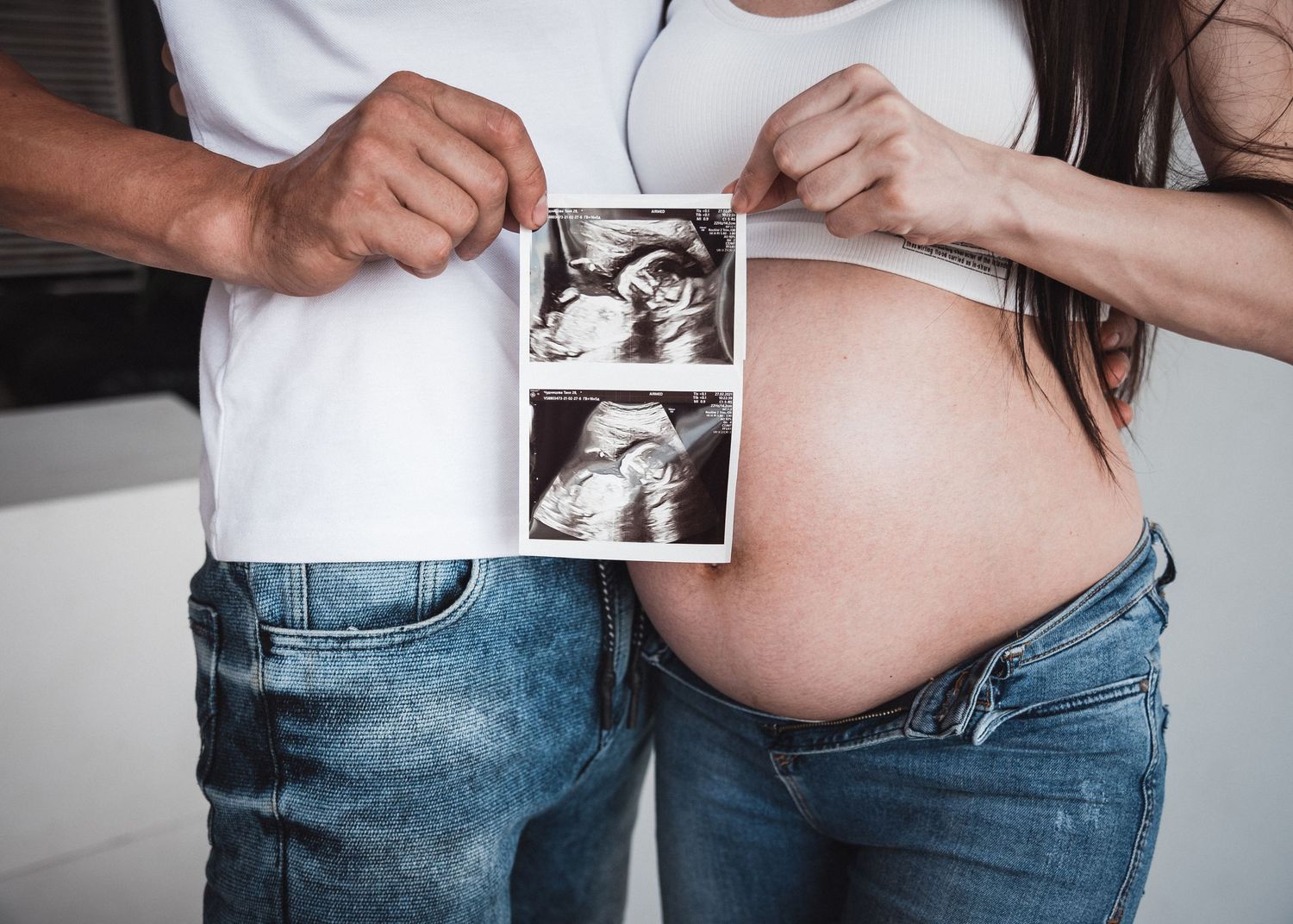Mains des futurs parents tenant une échographie devant le ventre de la future maman, séance grossesse en France