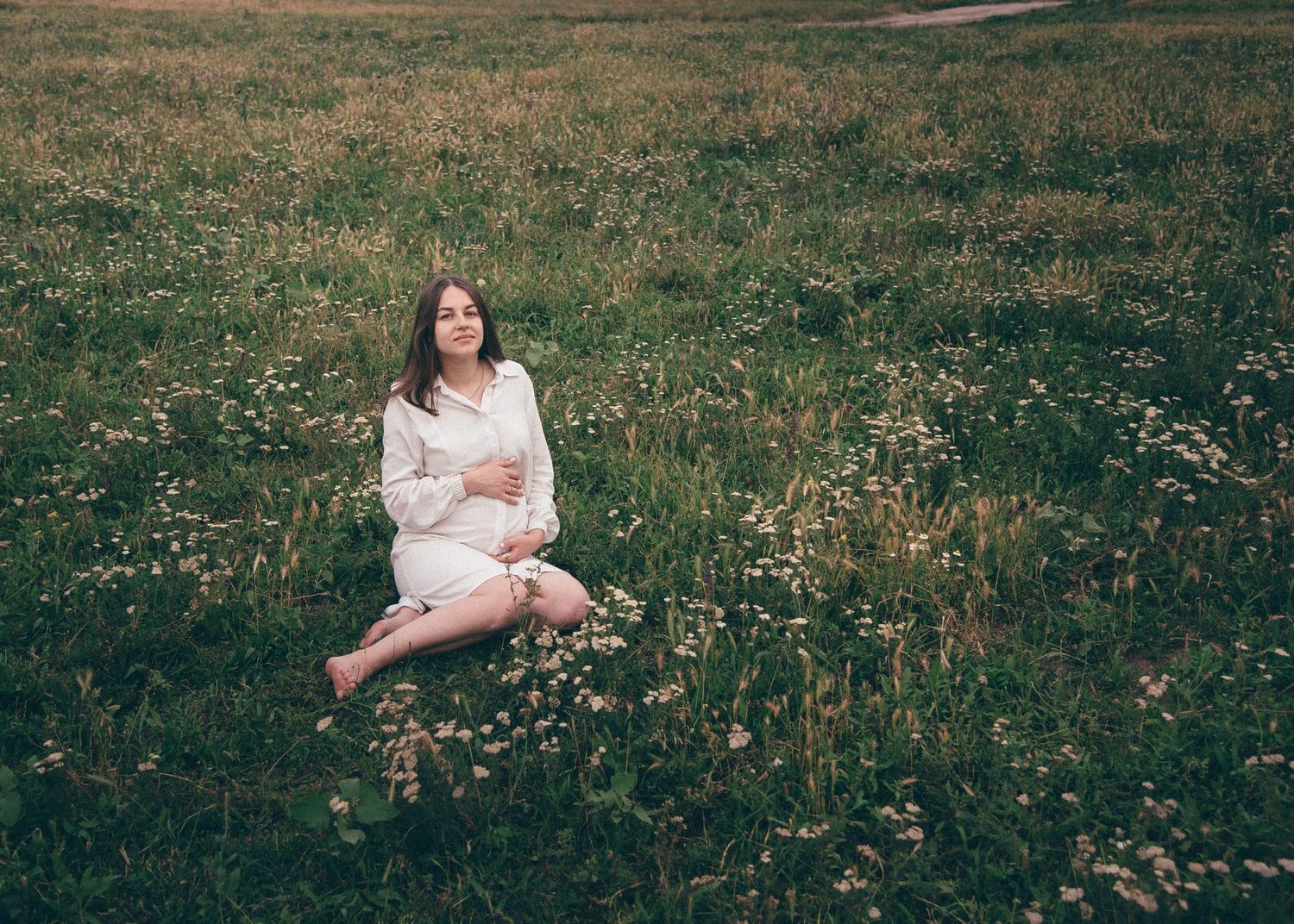 Femme enceinte assise dans un champ fleuri, photographie de maternité en lumière naturelle
