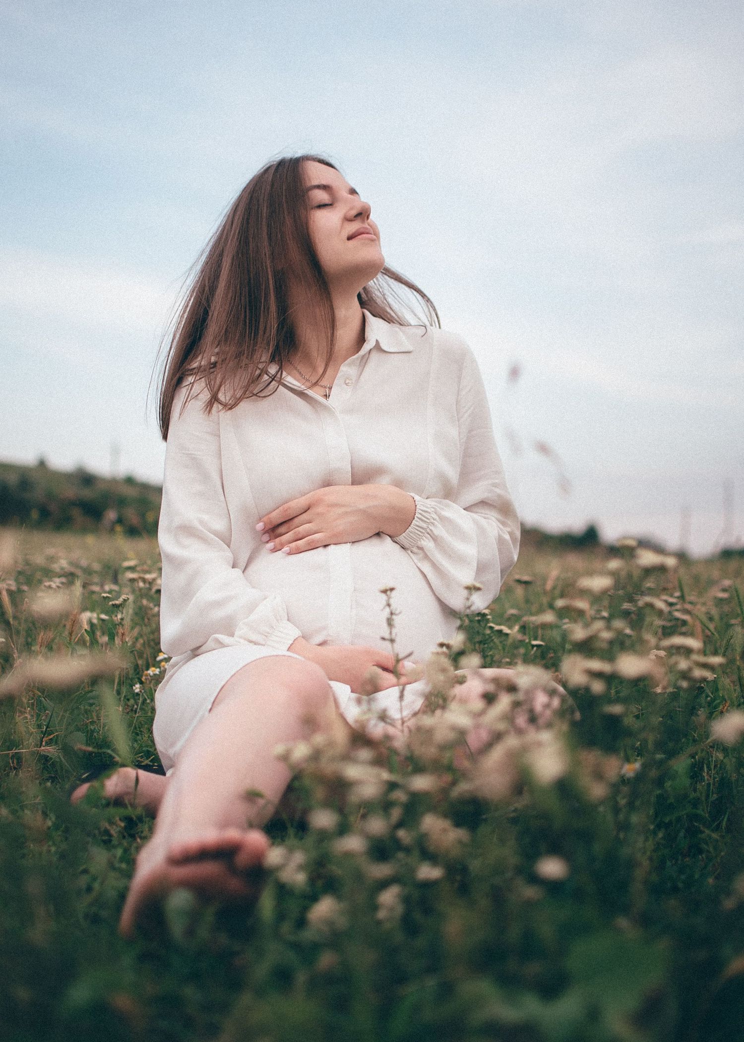 Femme enceinte assise dans l’herbe, séance photo maternité douce et naturelle