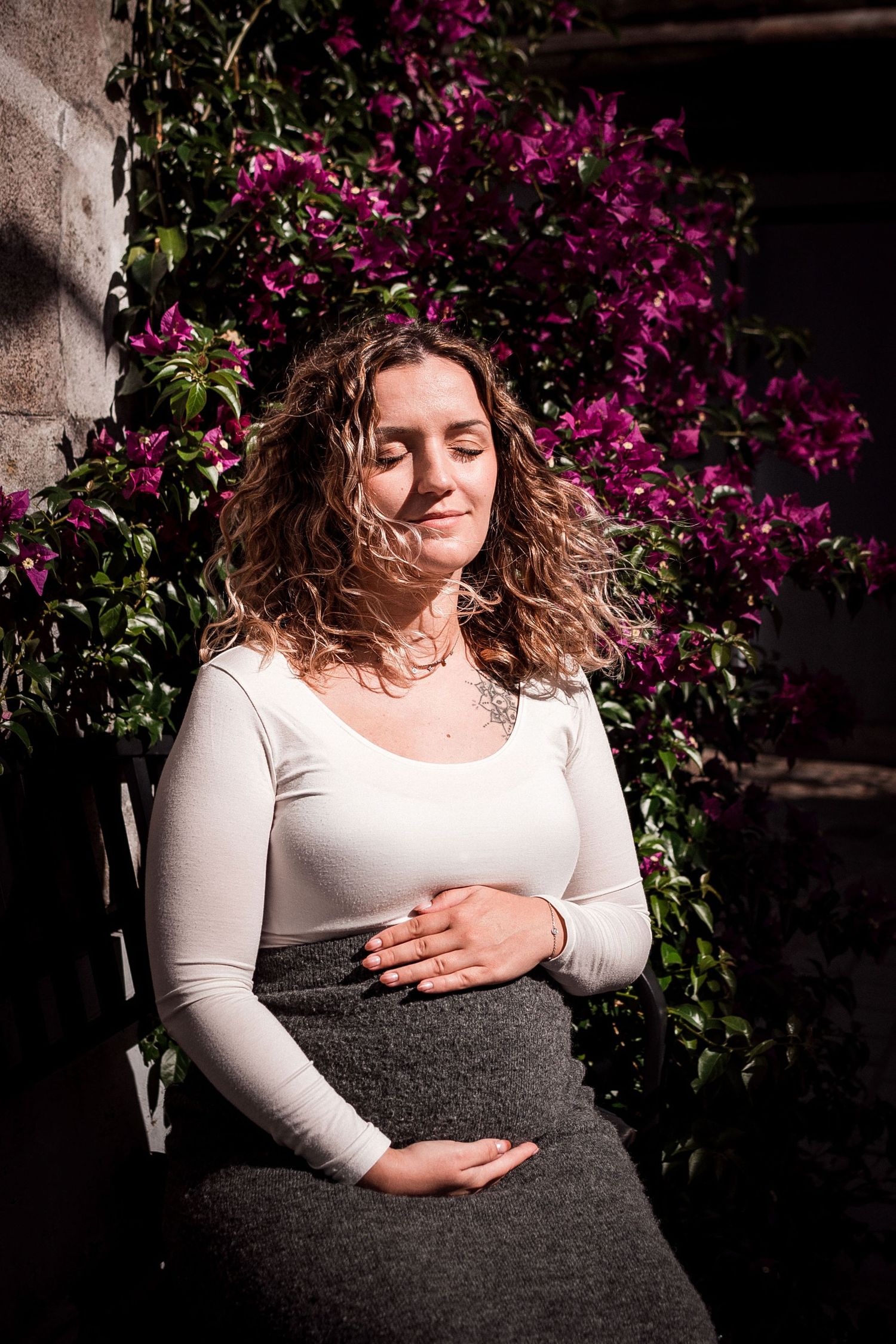 Femme enceinte les yeux fermés, moment de calme et de connexion devant une végétation fleurie à Guérande