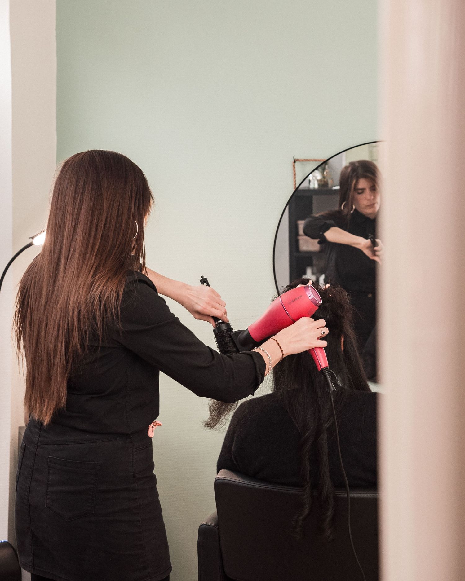 Coiffeuse en train de sécher les cheveux d’une cliente dans un salon, photographie lifestyle en lumière naturelle