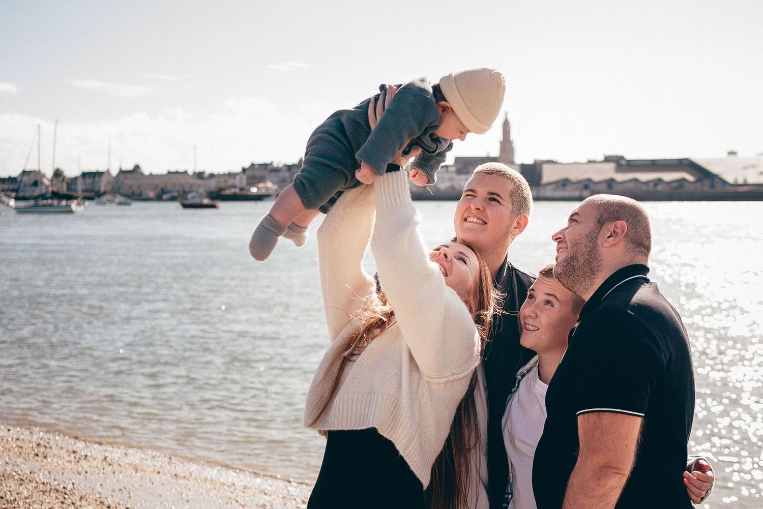 Famille levant un bébé en l’air près de l’eau, instant joyeux et spontané à Pen Bron