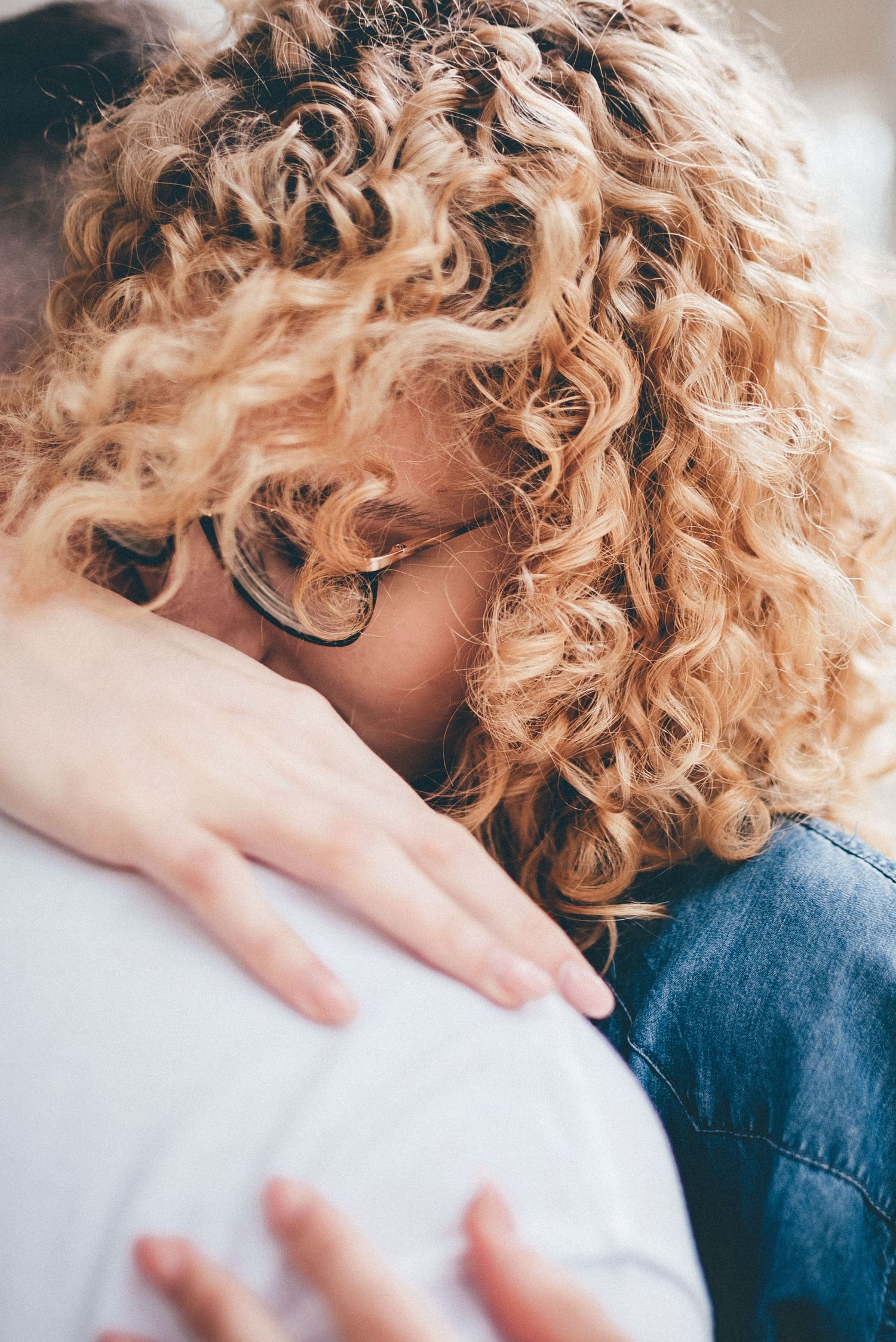 Close-up of curly blonde hair against white background in warm lighting.