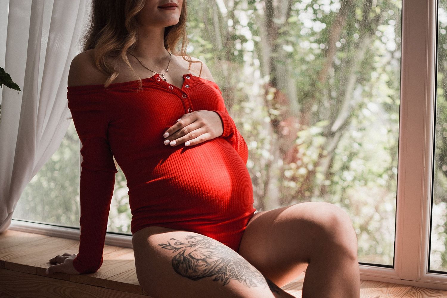 Femme enceinte assise près d’une fenêtre, séance photo maternité en lumière naturelle