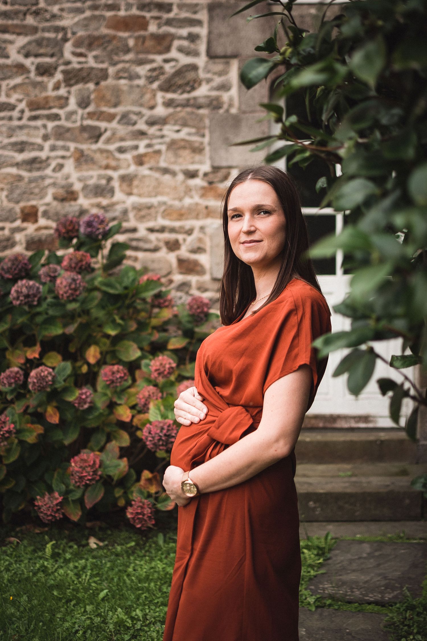 Portrait de femme enceinte en robe terracotta, pose naturelle dans un jardin fleuri à Guérande