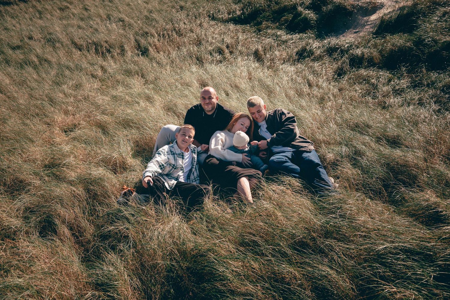 Portrait de famille assise dans les herbes hautes, ambiance naturelle et paysage ouvert à Pen Bron